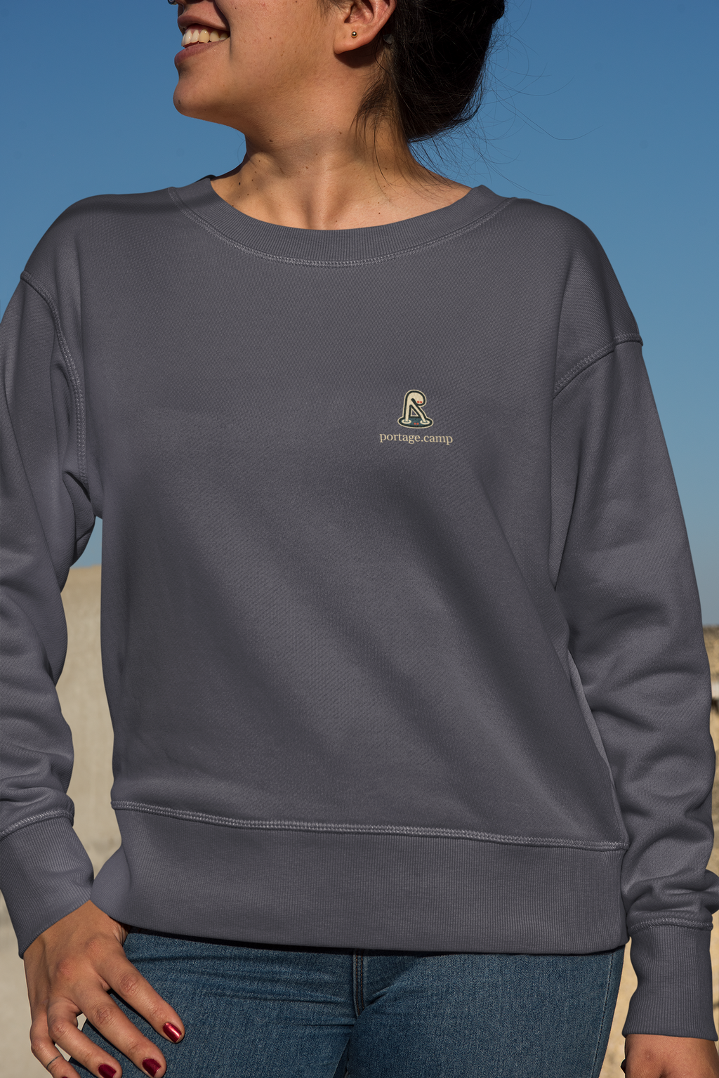 Small Hours Garment-Dyed Crewneck in Denim, worn by a woman against a plain backdrop, with the Small Hours logo and portage.camp on the chest. Digital product mockup.