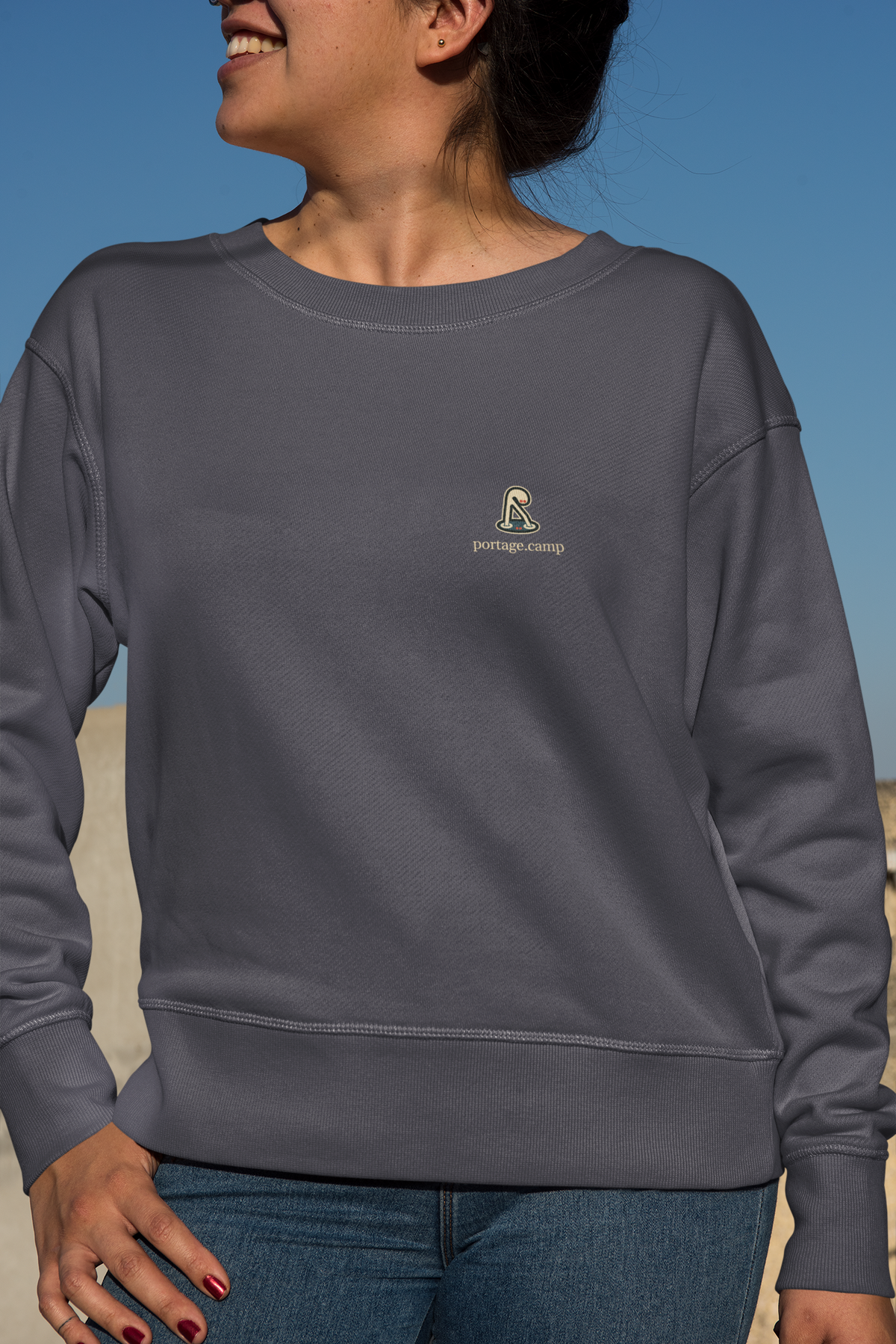 Small Hours Garment-Dyed Crewneck in Denim, worn by a woman against a plain backdrop, with the Small Hours logo and portage.camp on the chest. Digital product mockup.