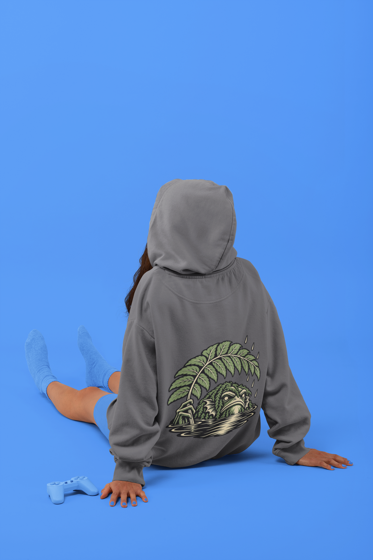 Rain Check Midweight Hoodie in Charcoal, worn by a woman seen from behind seated on a studio floor, showing the large print on the back. Digital product mockup.