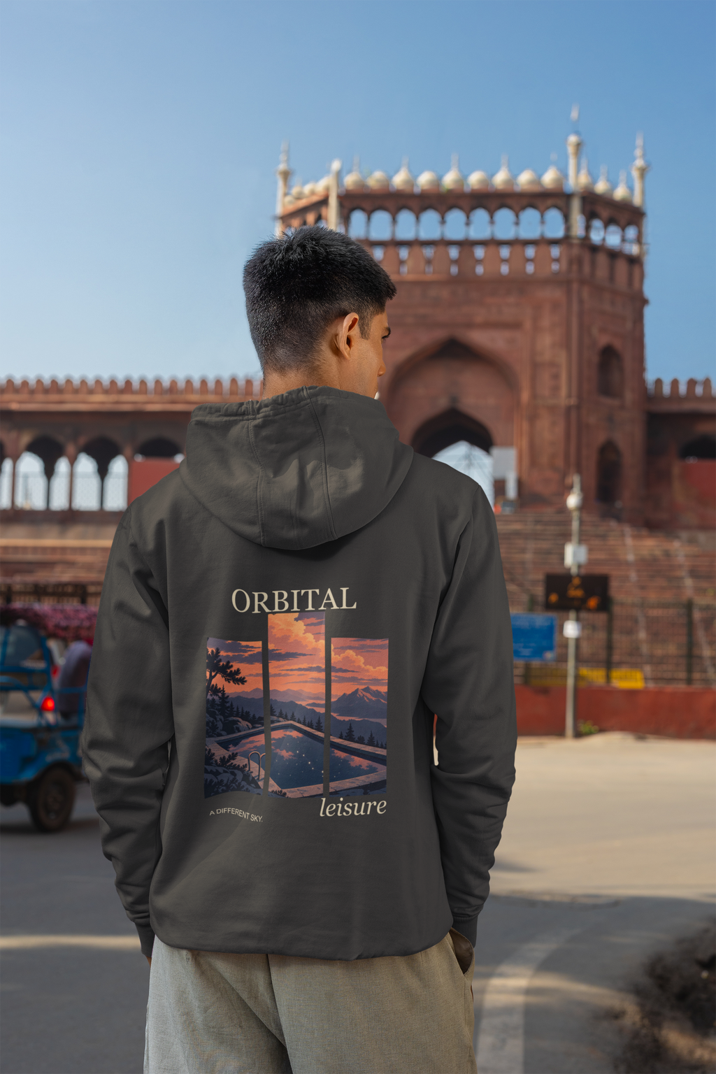 A Different Sky Heavyweight Hoodie in Black, worn by a man seen from behind on a city street, showing the large print on the back. Digital product mockup.