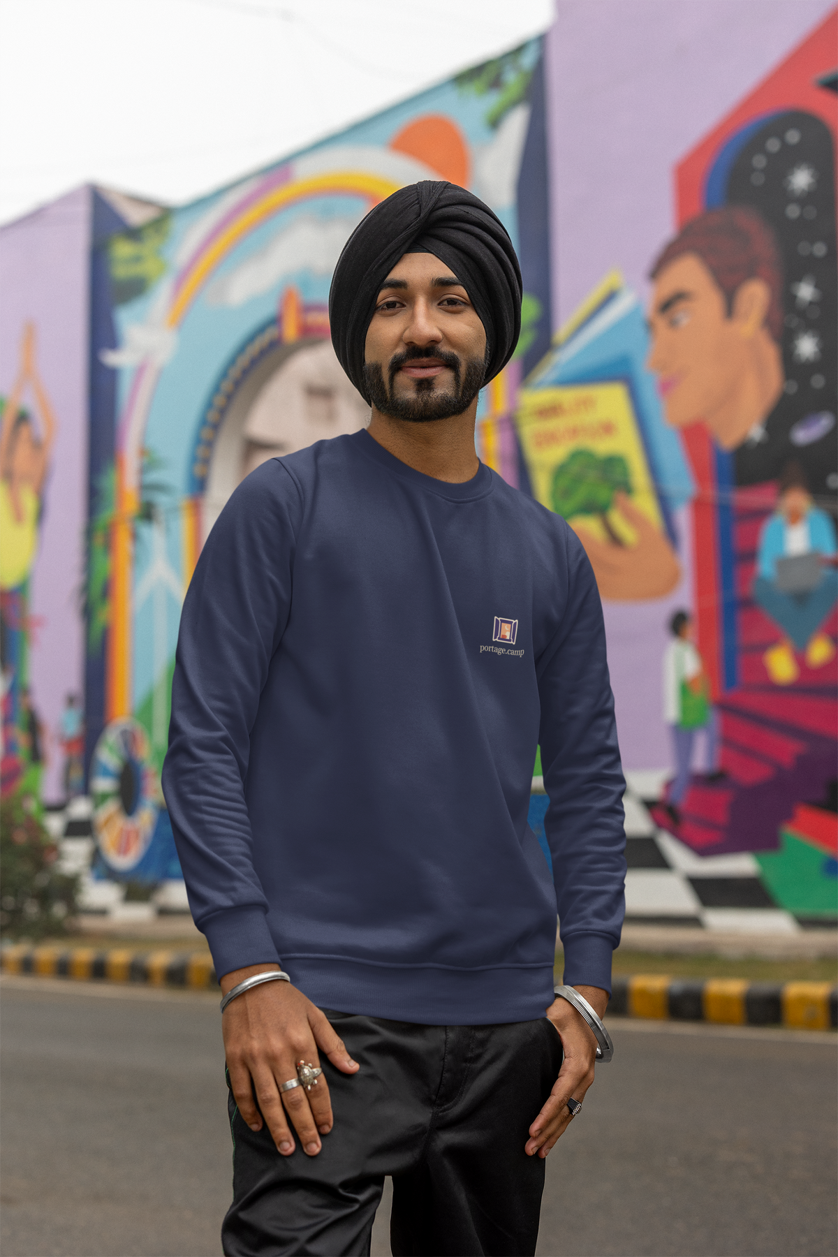 Open Late Garment-Dyed Crewneck in True Navy, worn by a man in a turban on a busy street, with the Open Late logo and portage.camp on the chest. Digital product mockup.
