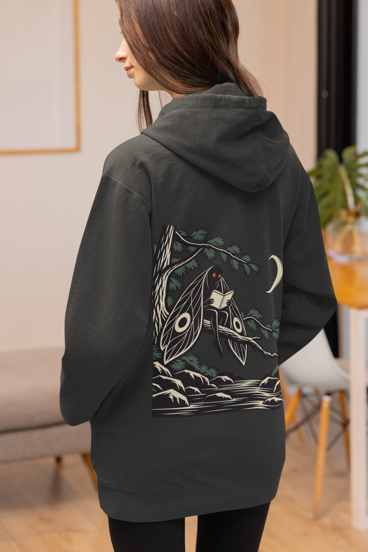 Night Library Zip Hoodie in Black, worn by a woman seen from behind at home, showing the large print on the back. Digital product mockup.