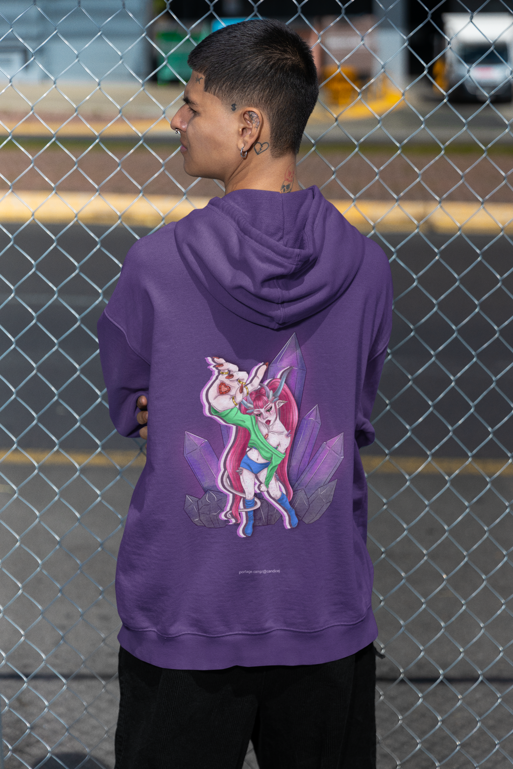 Amethyst After Hours Midweight Hoodie in Purple, worn by a man seen from behind by a chain-link fence, showing the large print on the back. Digital product mockup.