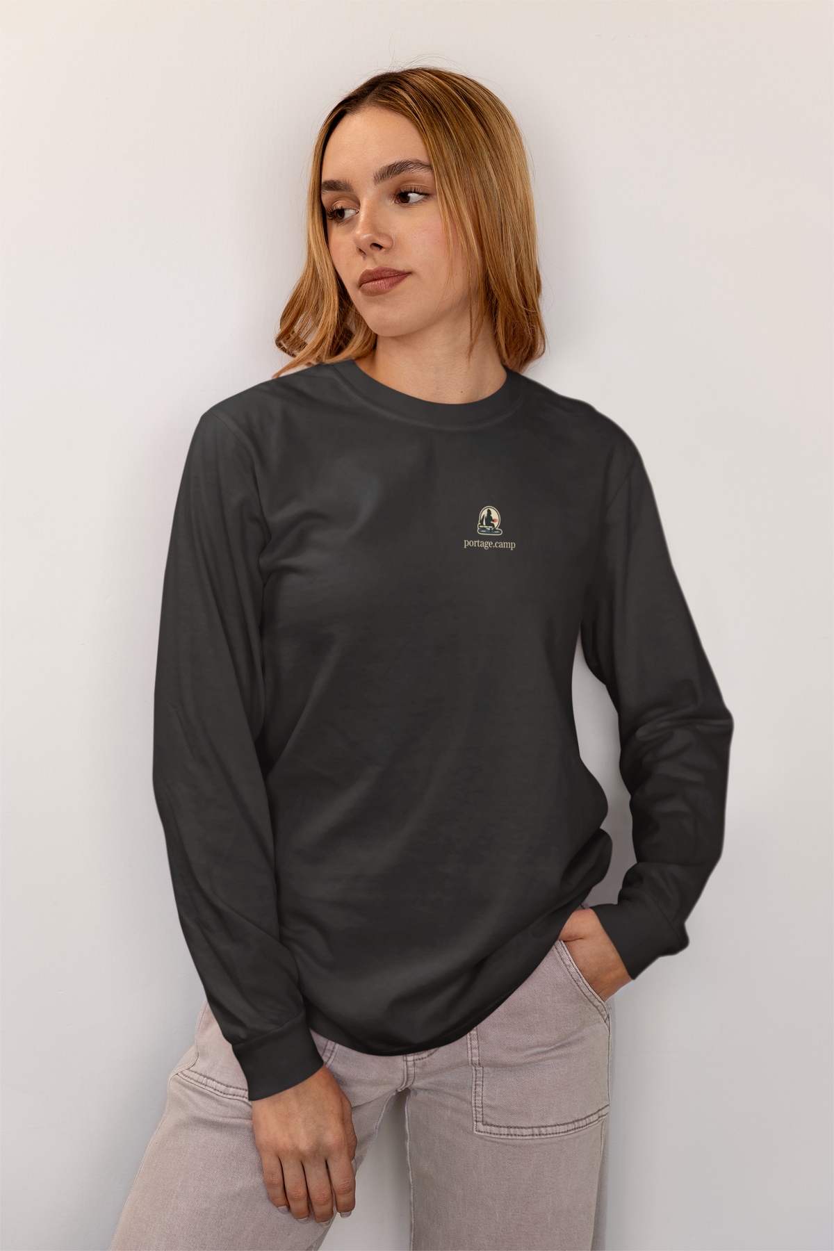 Quiet Hours Garment-Dyed Long-Sleeve Tee in Black, worn by a woman at home, with the Quiet Hours logo and portage.camp on the chest. Digital product mockup.