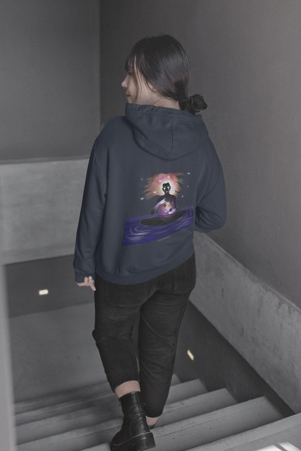 Orbit Keeper Zip Hoodie in Navy, worn by a woman seen from behind walking down a staircase, showing the large print on the back. Digital product mockup.