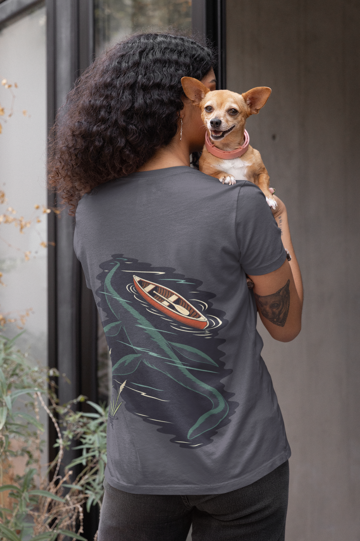 Seen Briefly Garment-Dyed Tee in Navy, worn by a woman seen from behind holding a small dog, showing the large print on the back. Digital product mockup.