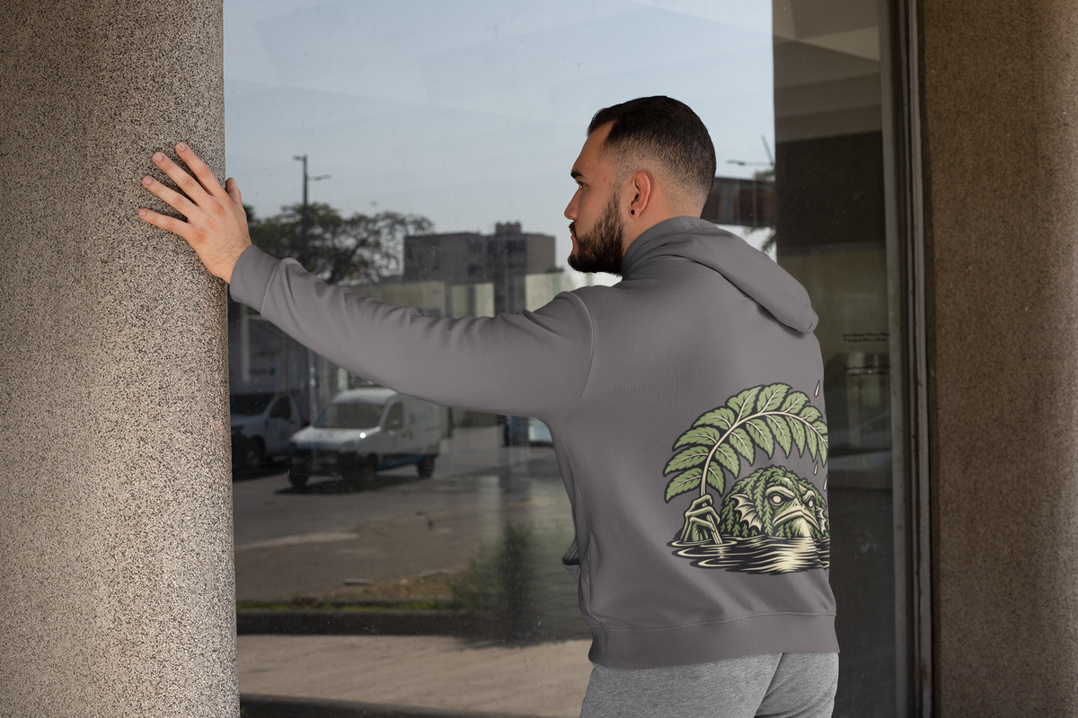 Rain Check Midweight Hoodie in Charcoal, worn by a man seen from behind leaning on a pillar by a window, showing the large print on the back. Digital product mockup.