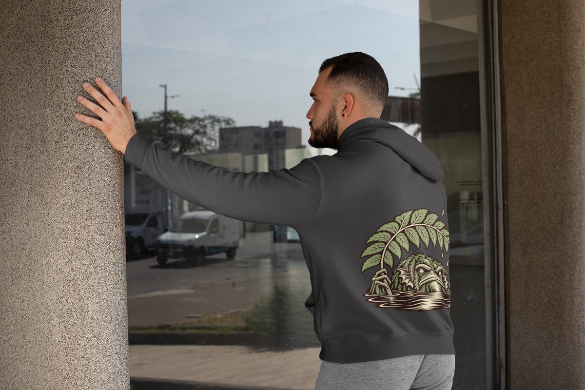 Rain Check Heavyweight Hoodie in Black, worn by a man seen from behind leaning on a pillar by a window, showing the large print on the back. Digital product mockup.