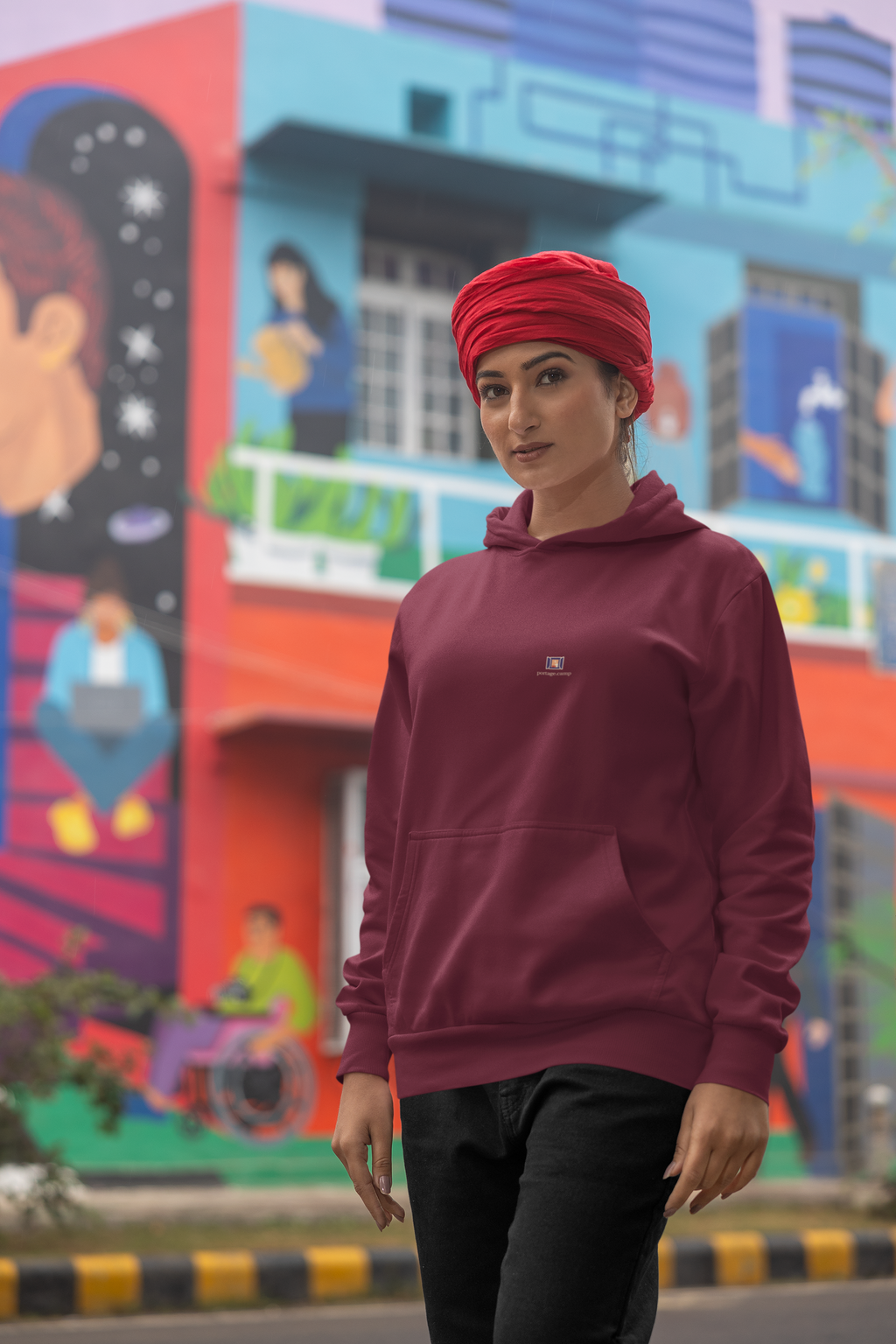 Open Late Midweight Hoodie in Maroon, worn by a woman in a turban on a busy street, with the Open Late logo and portage.camp on the chest. Digital product mockup.