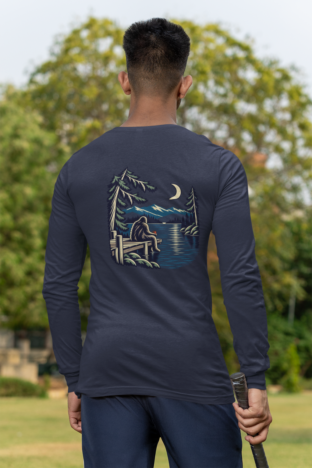 Quiet Hours Garment-Dyed Long-Sleeve Tee in True Navy, worn by a man seen from behind at a cricket field, showing the large print on the back. Digital product mockup.