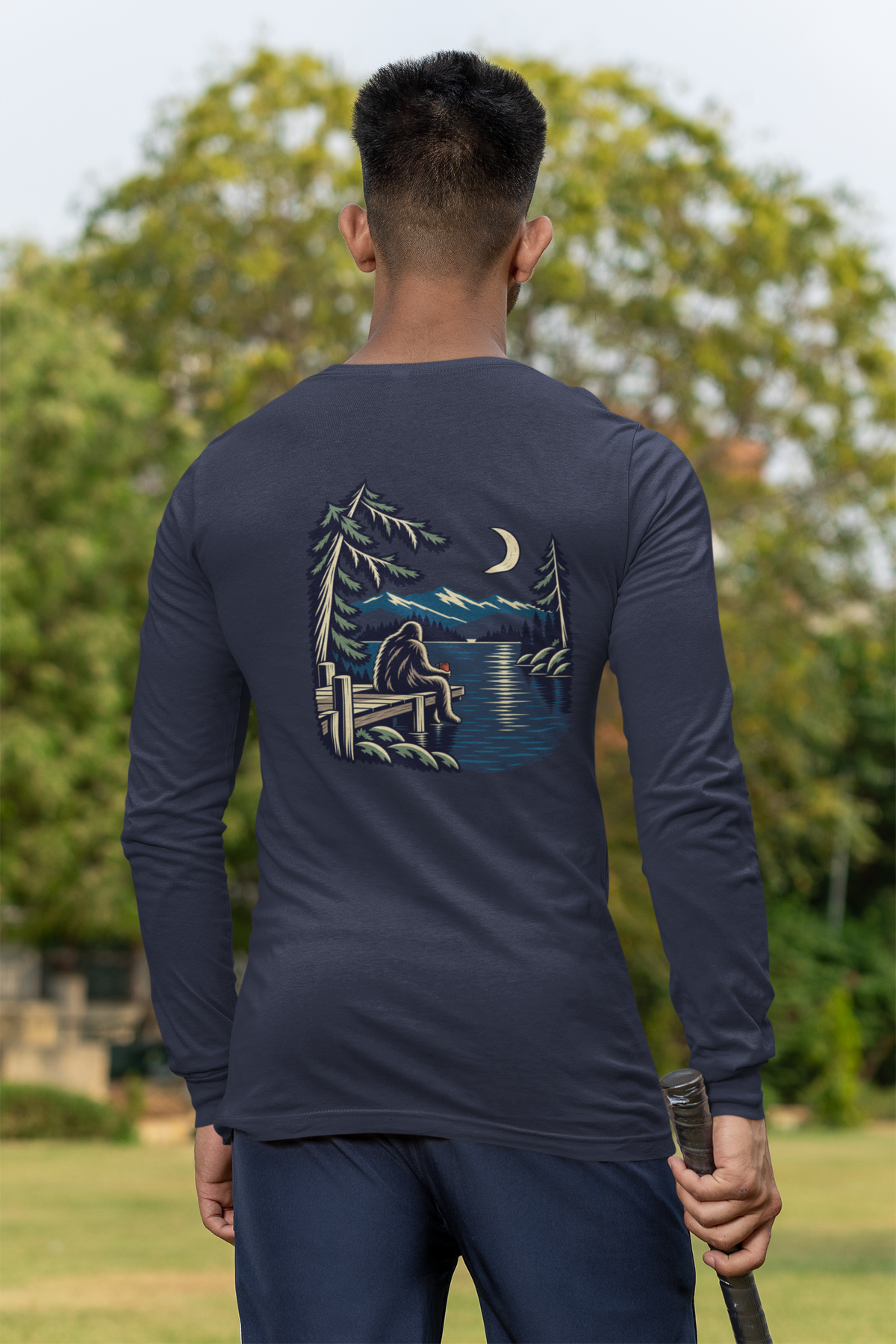 Quiet Hours Garment-Dyed Long-Sleeve Tee in True Navy, worn by a man seen from behind at a cricket field, showing the large print on the back. Digital product mockup.