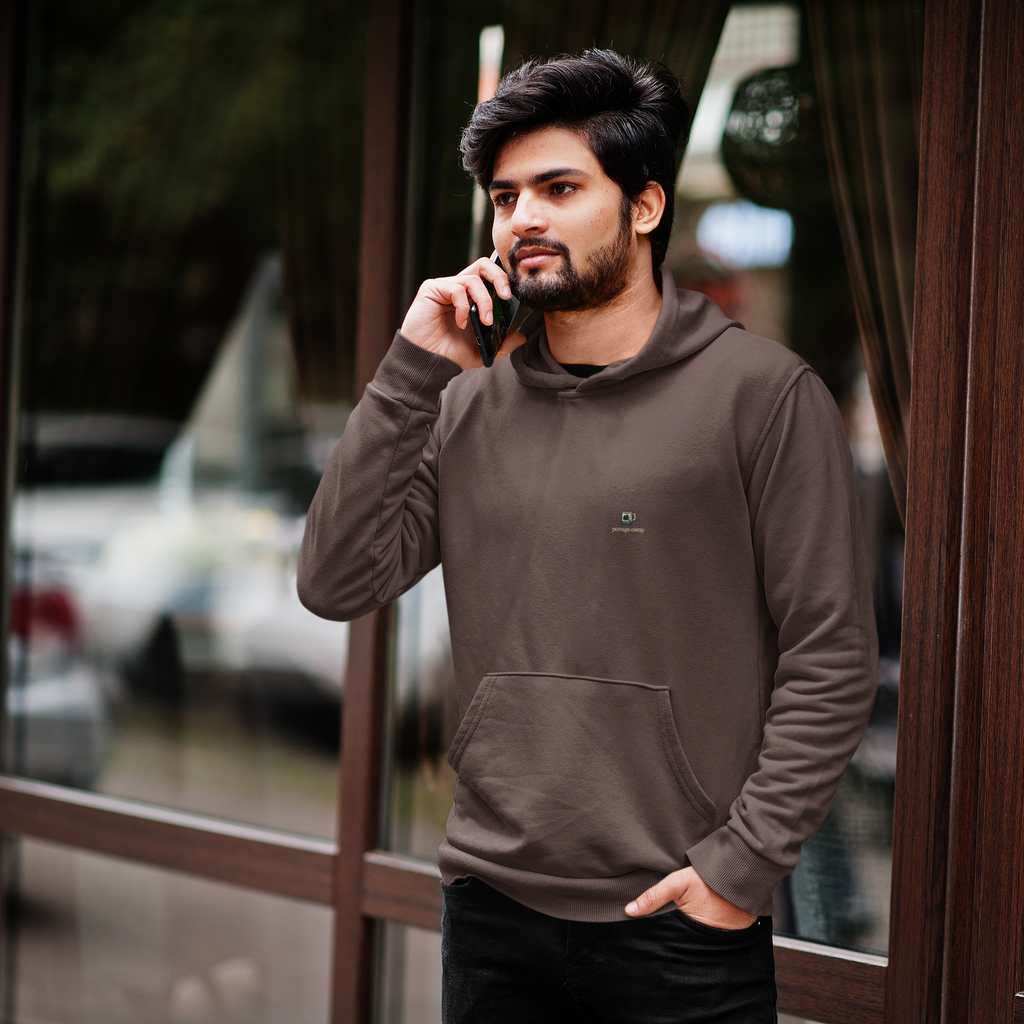 Quiet Hours Heavyweight Hoodie in Brown, worn by a man by a café window, on a phone call, with the Quiet Hours logo and portage.camp on the left chest. Digital product mockup.