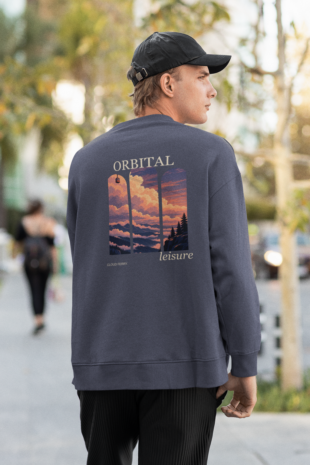 Cloud Ferry Garment-Dyed Crewneck in Denim, worn by a man seen from behind walking down a city street, showing the large print on the back. Digital product mockup.