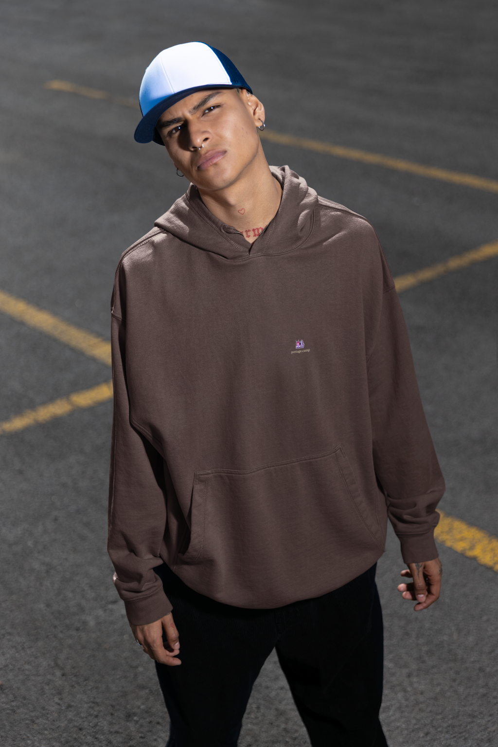 Amethyst After Hours Heavyweight Hoodie in Brown, worn by a man in a parking lot, with the Amethyst After Hours logo and portage.camp on the left chest. Digital product mockup.