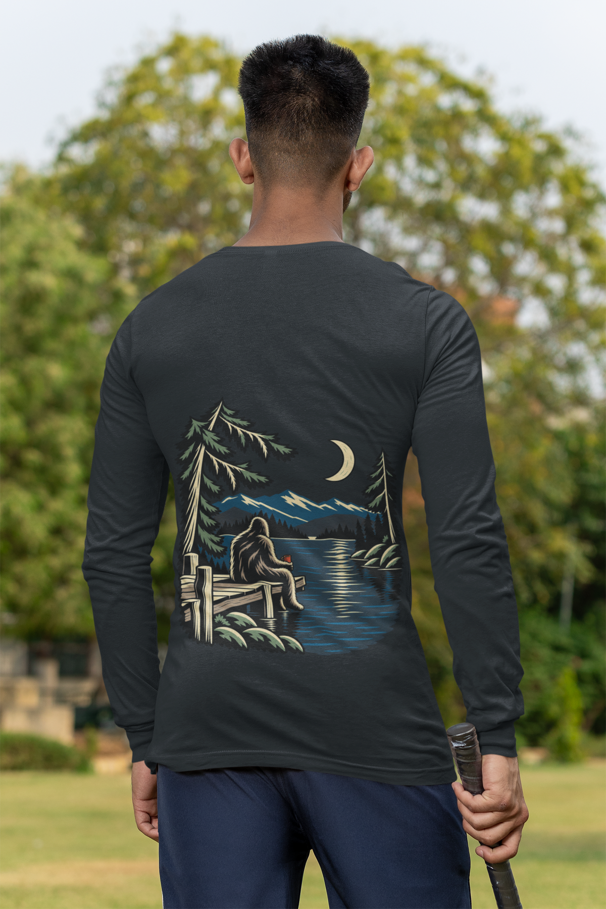 Quiet Hours Garment-Dyed Long-Sleeve Tee in Black, worn by a man seen from behind at a cricket field, showing the large print on the back. Digital product mockup.