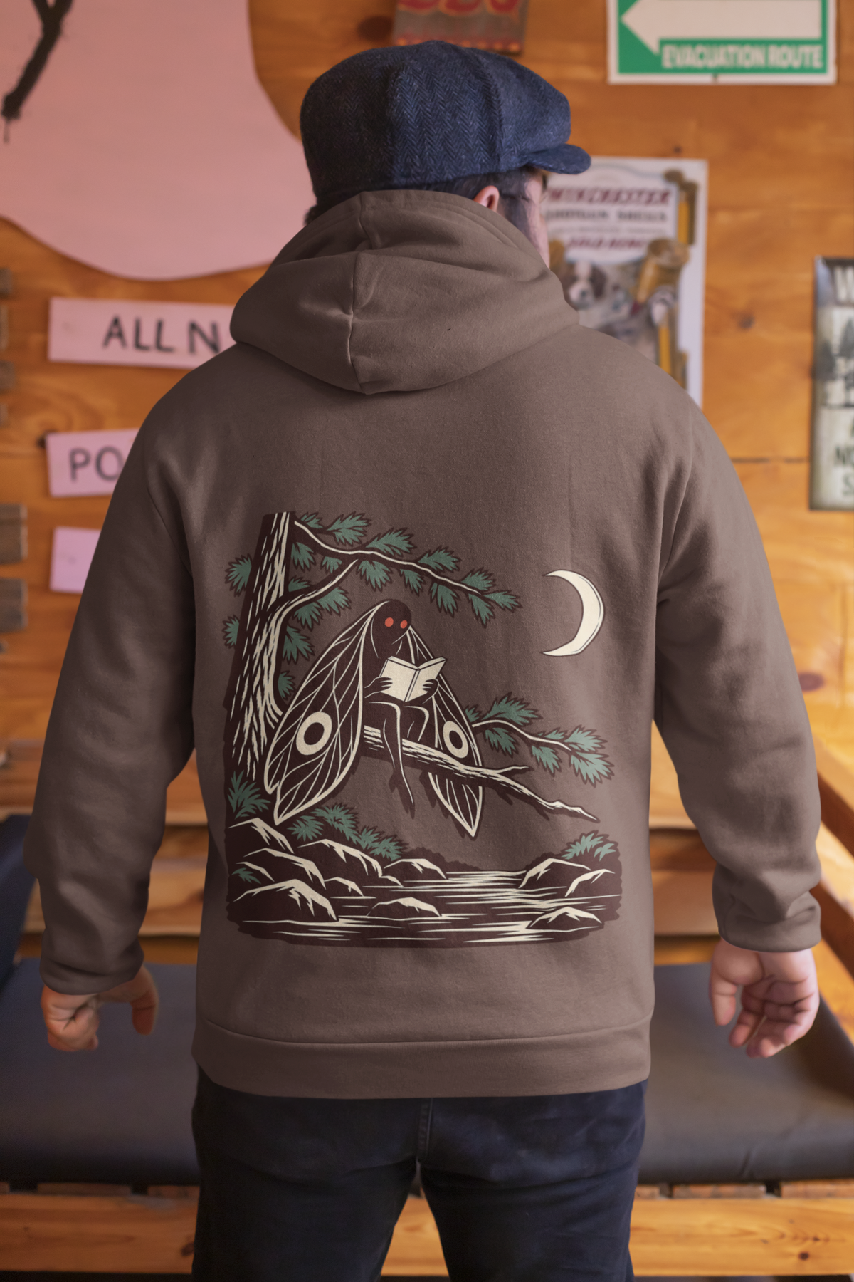 Night Library Heavyweight Hoodie in Brown, worn by a man seen from behind in a wood-panelled bar, showing the large print on the back. Digital product mockup.