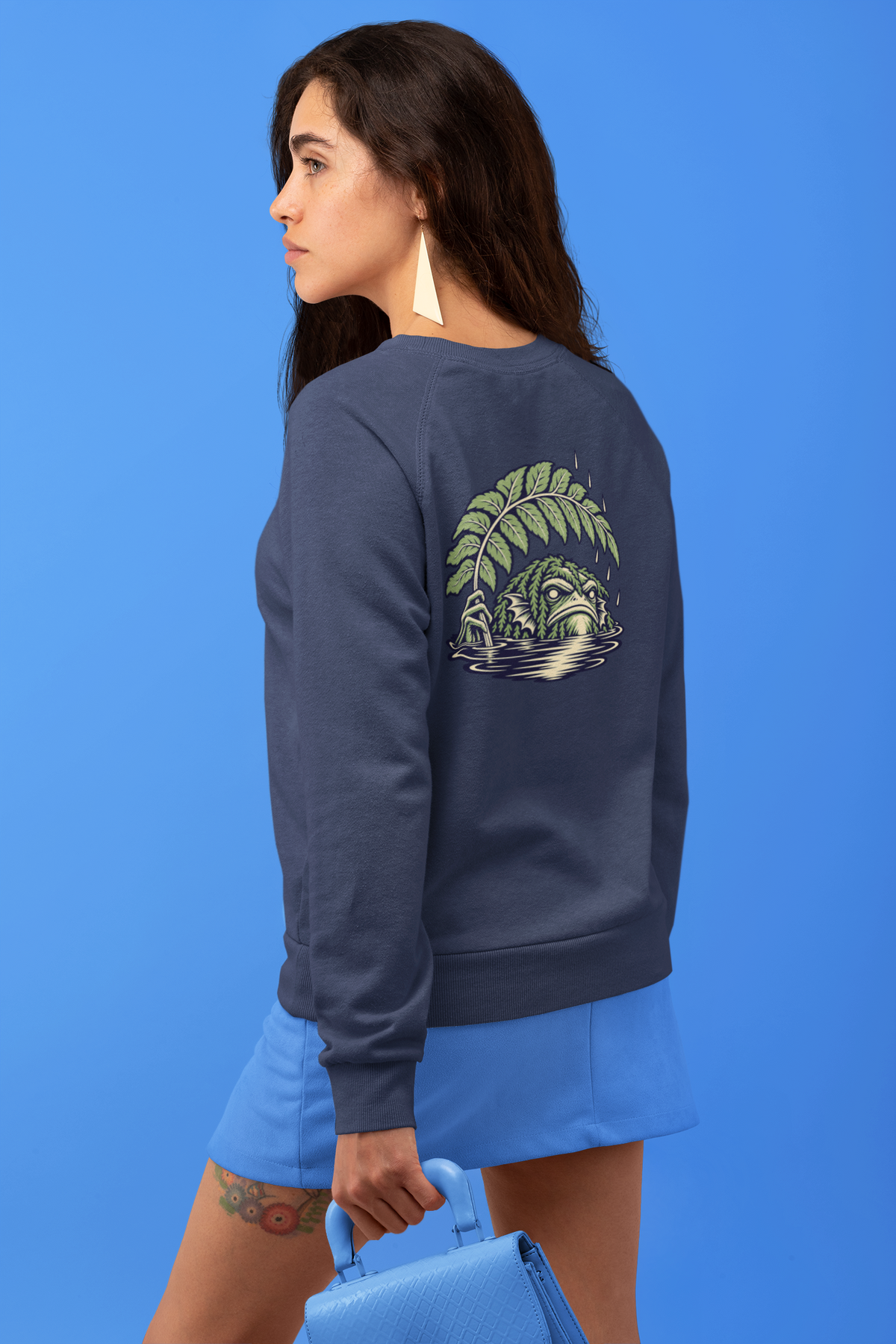 Rain Check Garment-Dyed Crewneck in True Navy, worn by a woman seen from behind against a blue backdrop, showing the large print on the back. Digital product mockup.