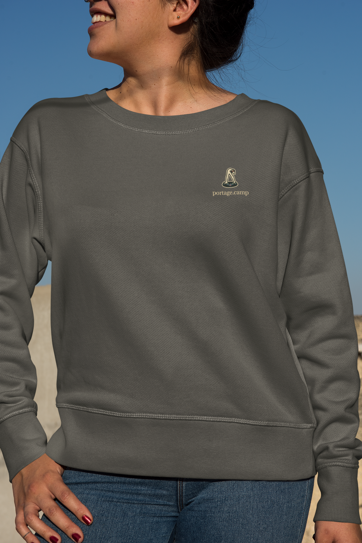 Small Hours Garment-Dyed Crewneck in Pepper, worn by a woman against a plain backdrop, with the Small Hours logo and portage.camp on the chest. Digital product mockup.