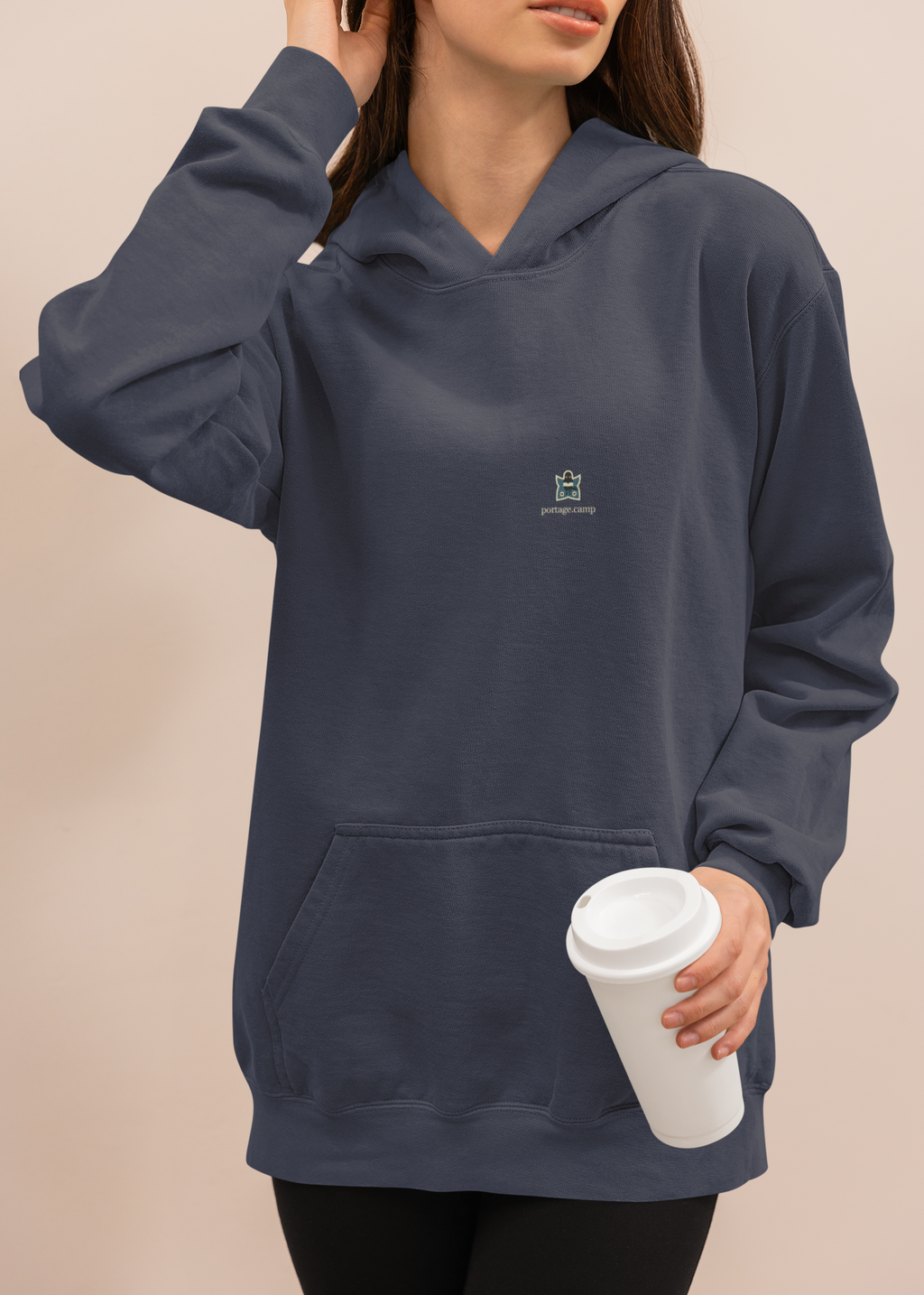 Night Library Midweight Hoodie in Classic Navy, worn by a woman at home with a coffee cup, with the Night Library logo and portage.camp on the chest. Digital product mockup.