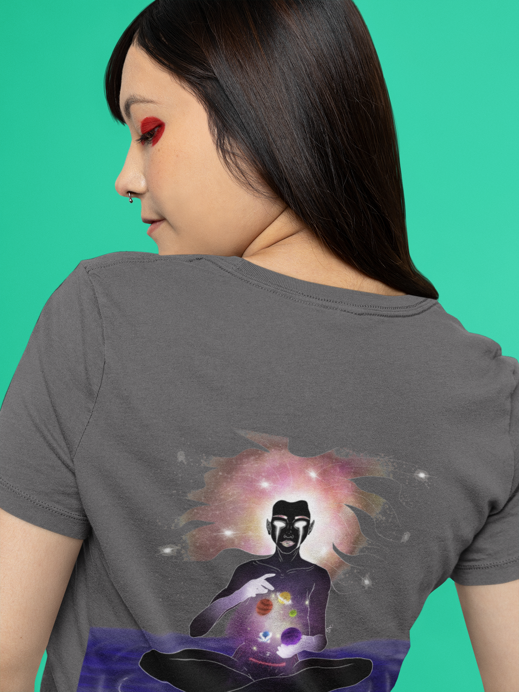 Orbit Keeper Garment-Dyed Tee in Graphite, worn by a woman seen from behind against green, showing the large print on the back. Digital product mockup.