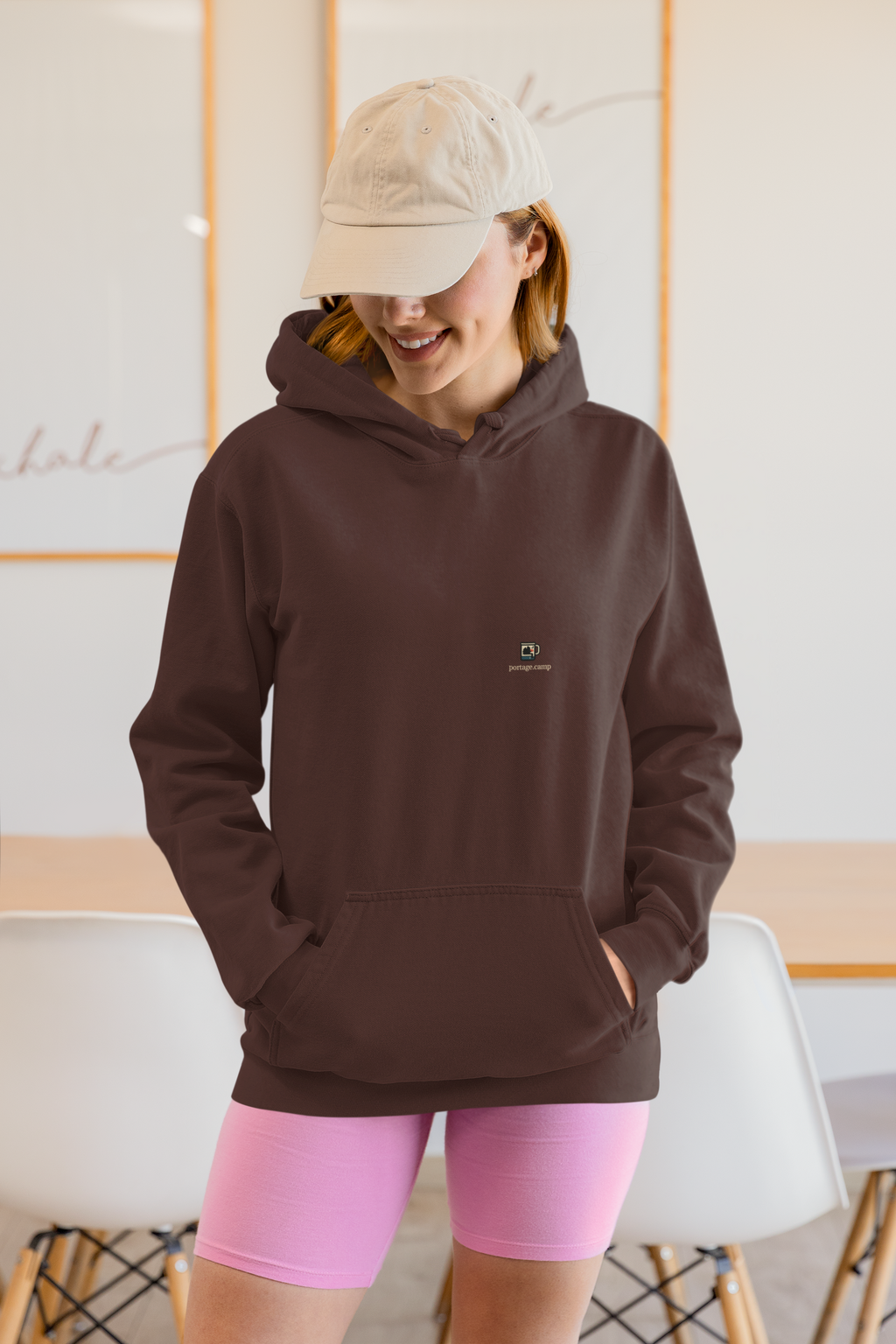 Quiet Hours Heavyweight Hoodie in Brown, worn by a woman at home, with the Quiet Hours logo and portage.camp on the left chest. Digital product mockup.