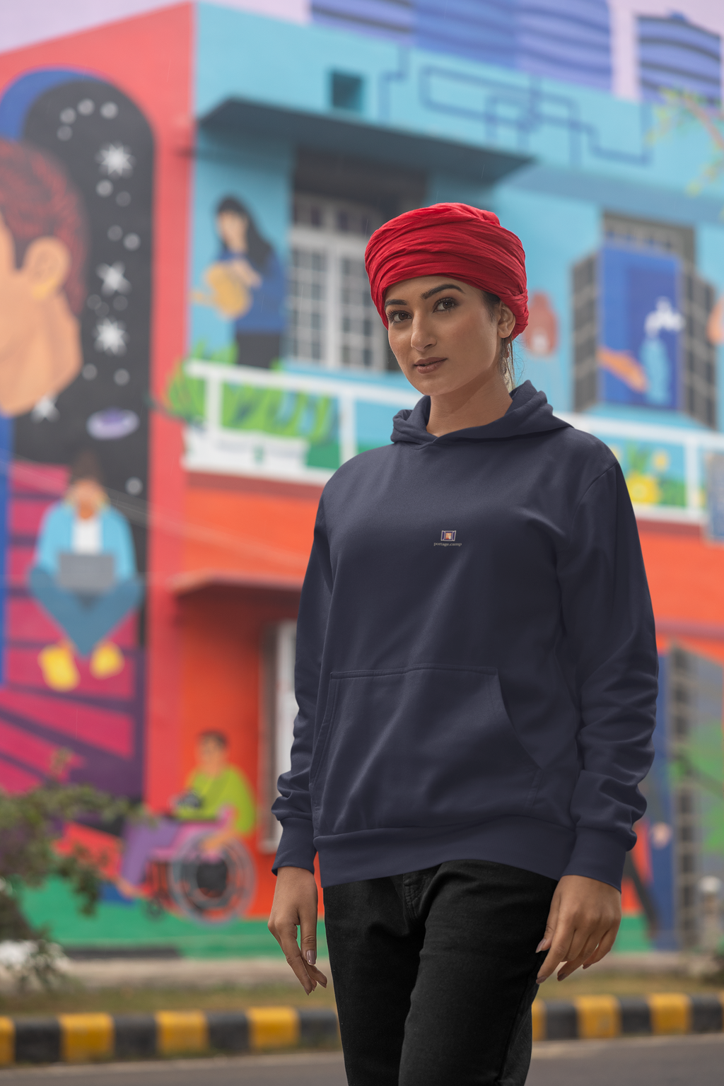 Open Late Midweight Hoodie in Classic Navy, worn by a woman in a turban on a busy street, with the Open Late logo and portage.camp on the chest. Digital product mockup.
