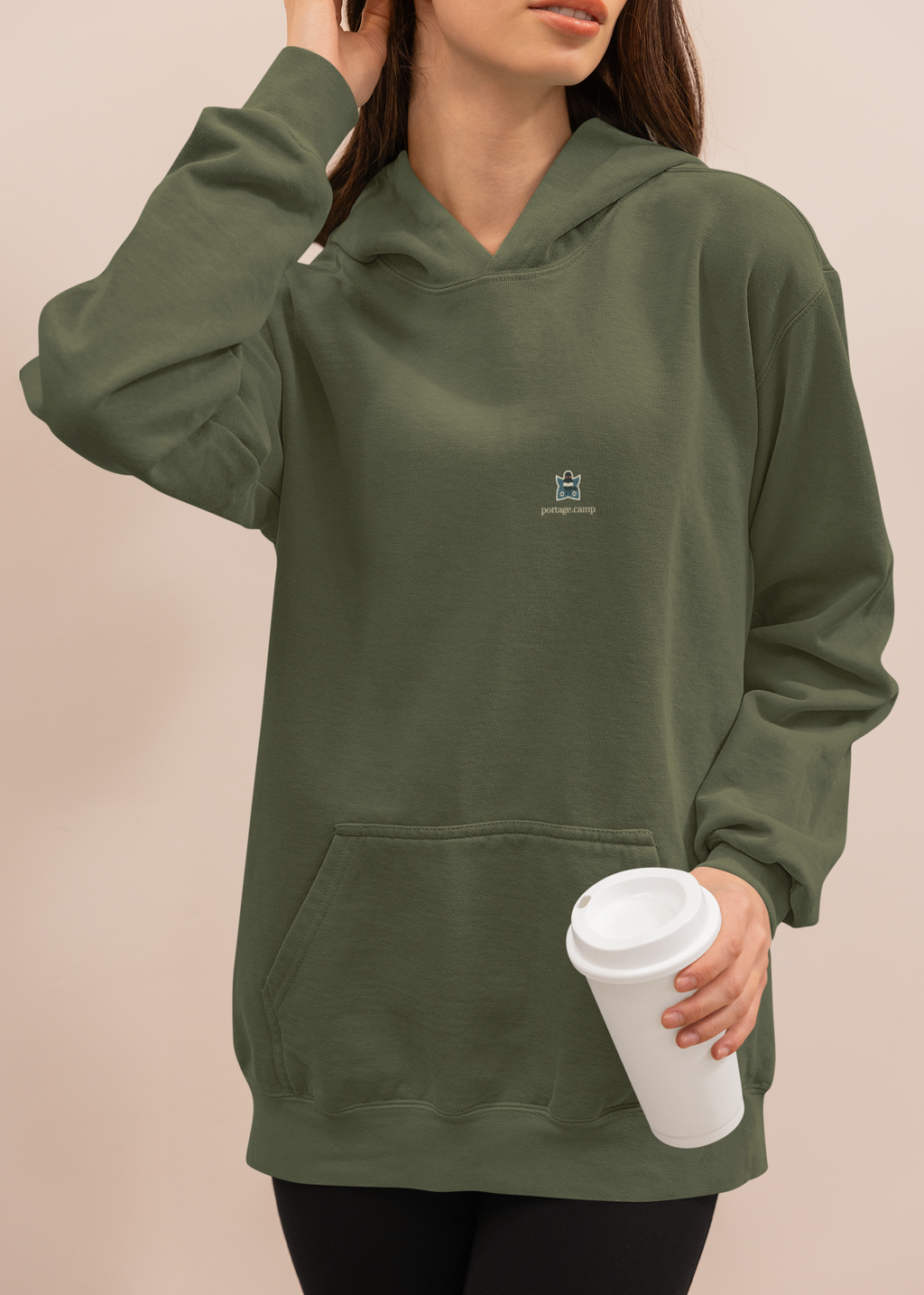 Night Library Midweight Hoodie in Army, worn by a woman at home with a coffee cup, with the Night Library logo and portage.camp on the chest. Digital product mockup.