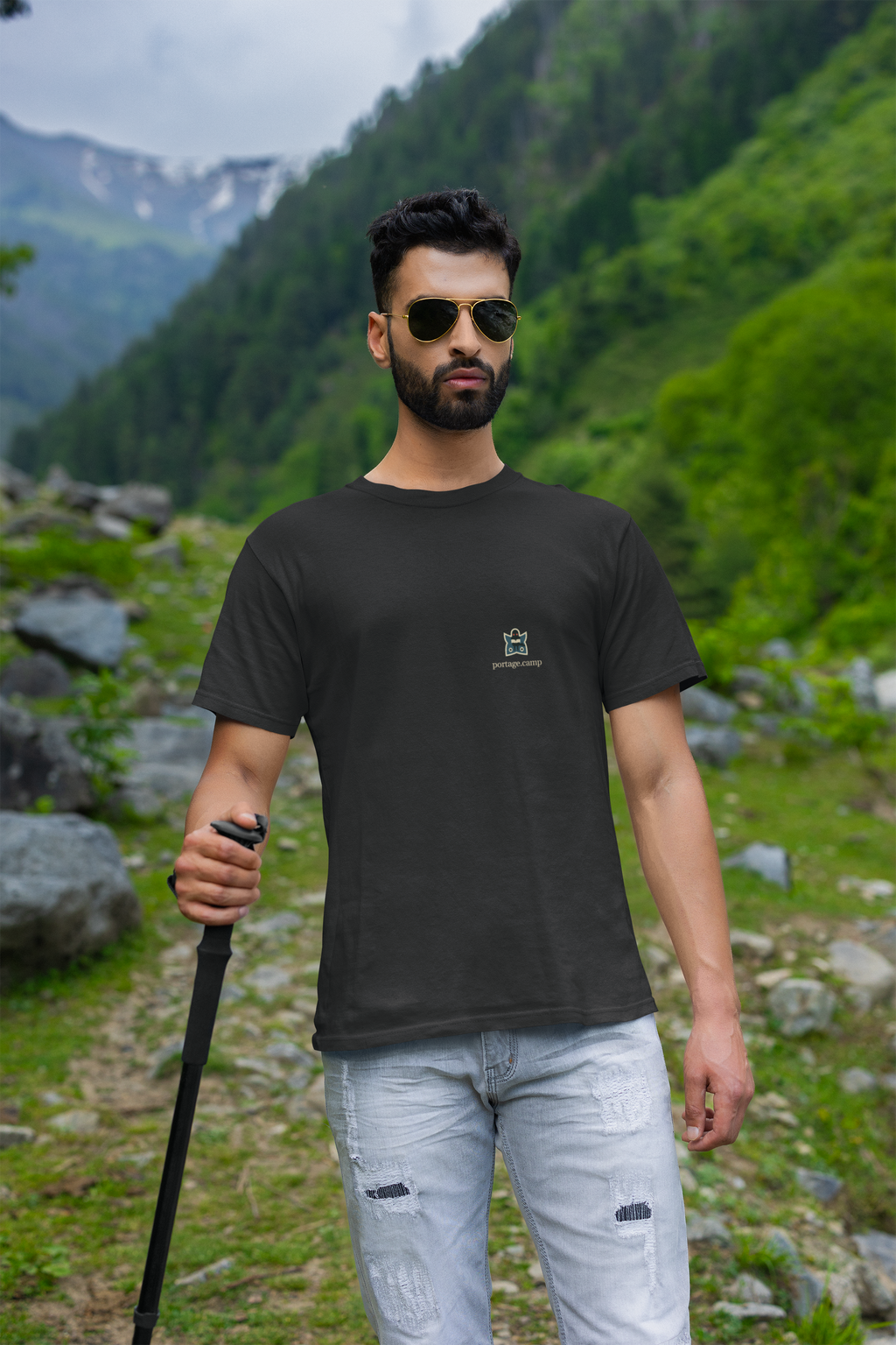 Night Library Garment-Dyed Tee in Black, worn by a man on a mountain trail, with the Night Library logo and portage.camp on the chest. Digital product mockup.