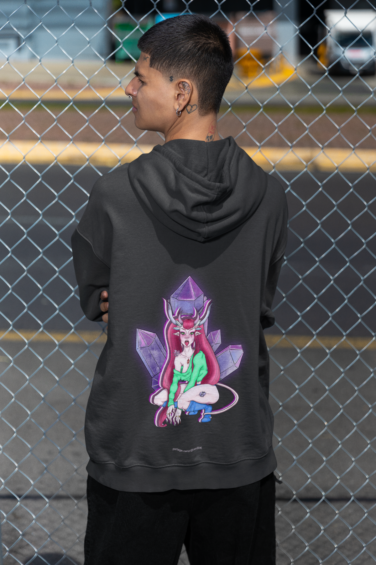 Amethyst After Hours Heavyweight Hoodie in Black, worn by a man seen from behind by a chain-link fence, showing the large print on the back. Digital product mockup.