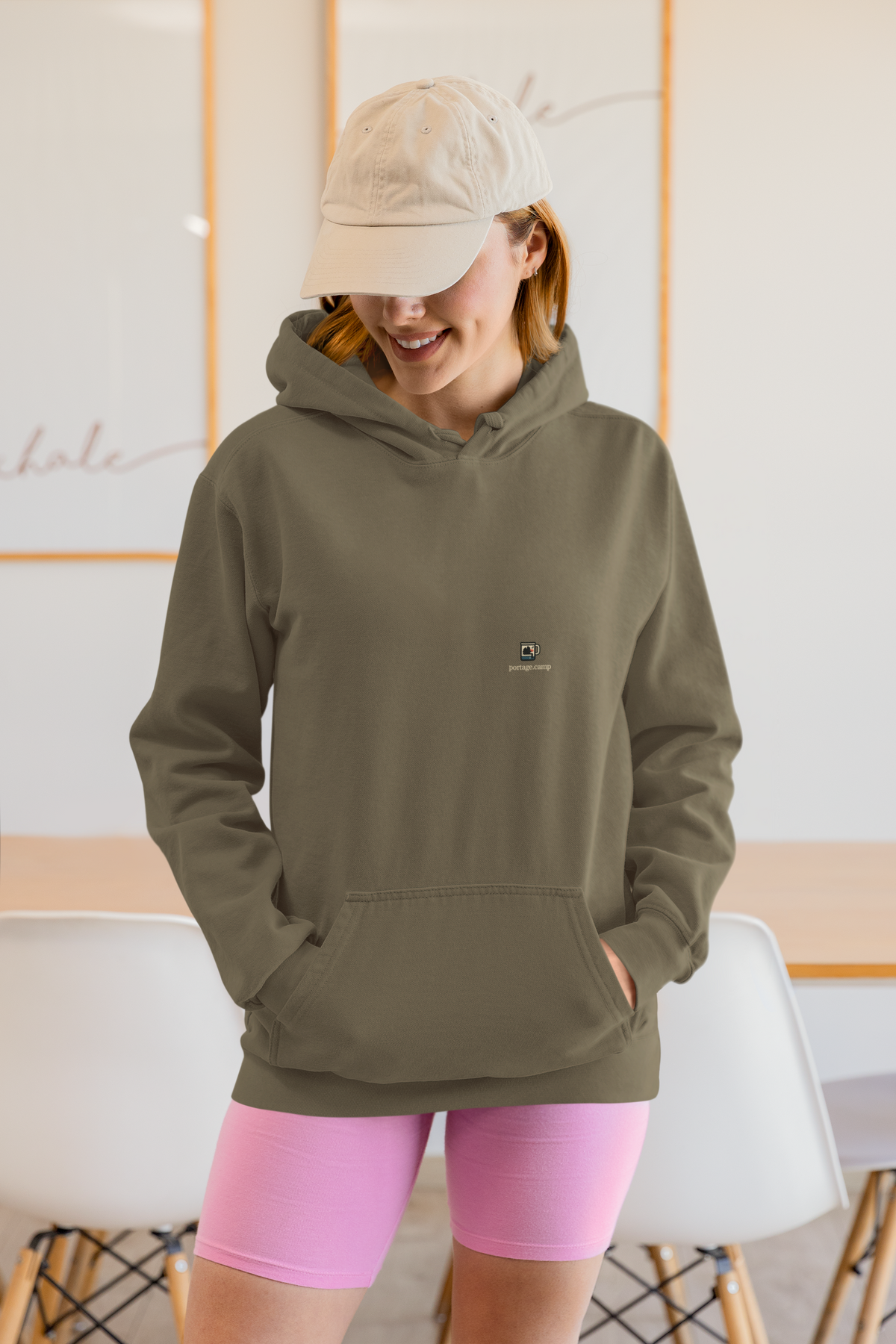 Quiet Hours Heavyweight Hoodie in Olive, worn by a woman at home, with the Quiet Hours logo and portage.camp on the left chest. Digital product mockup.