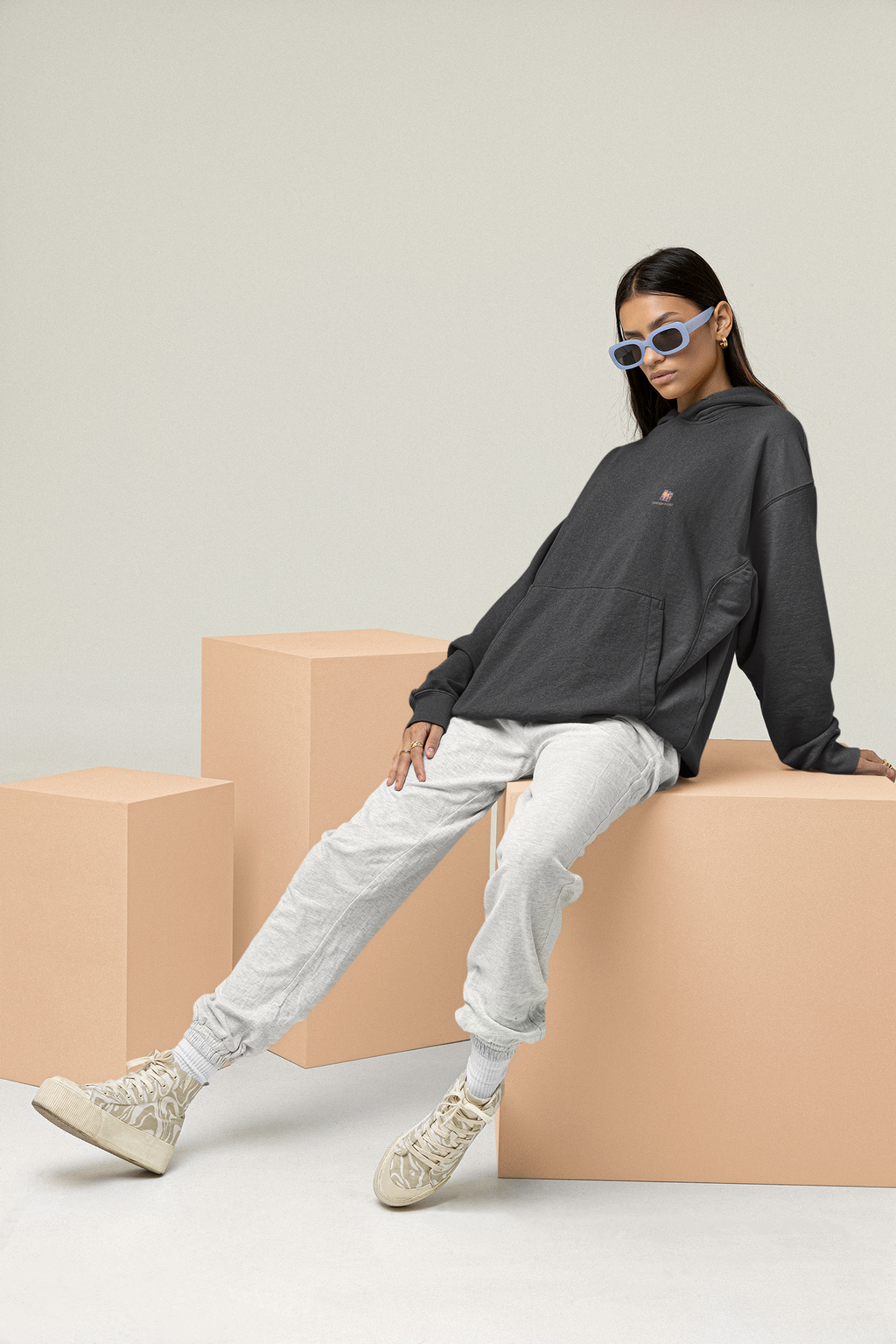 Stay for the Sky Heavyweight Hoodie in Black, worn by a woman leaning back on studio blocks, with the Stay for the Sky logo and portage.camp on the left chest. Digital product mockup.