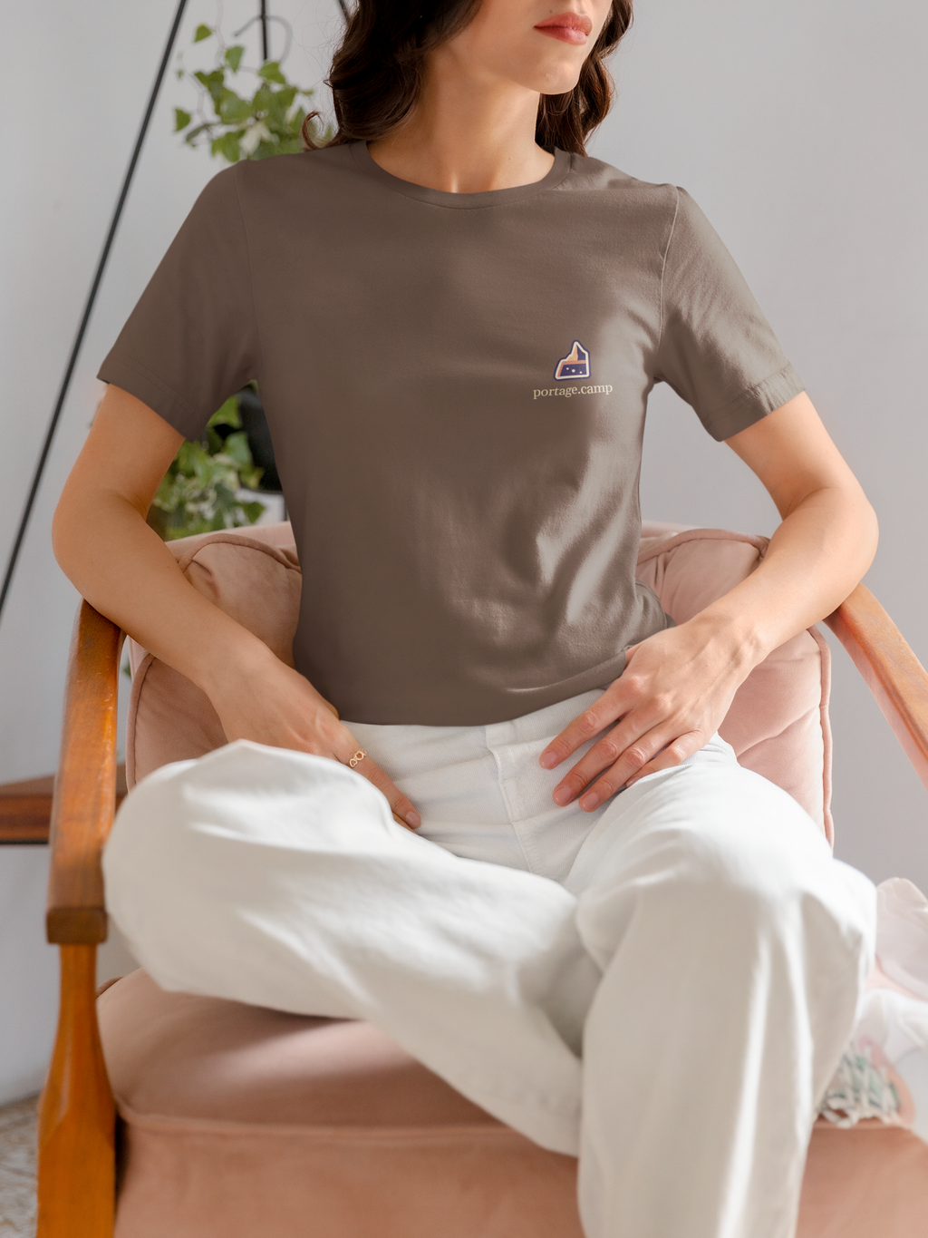 A Different Sky Garment-Dyed Tee in Espresso, worn by a woman seated on a chair at home, with the A Different Sky logo and portage.camp on the chest. Digital product mockup.