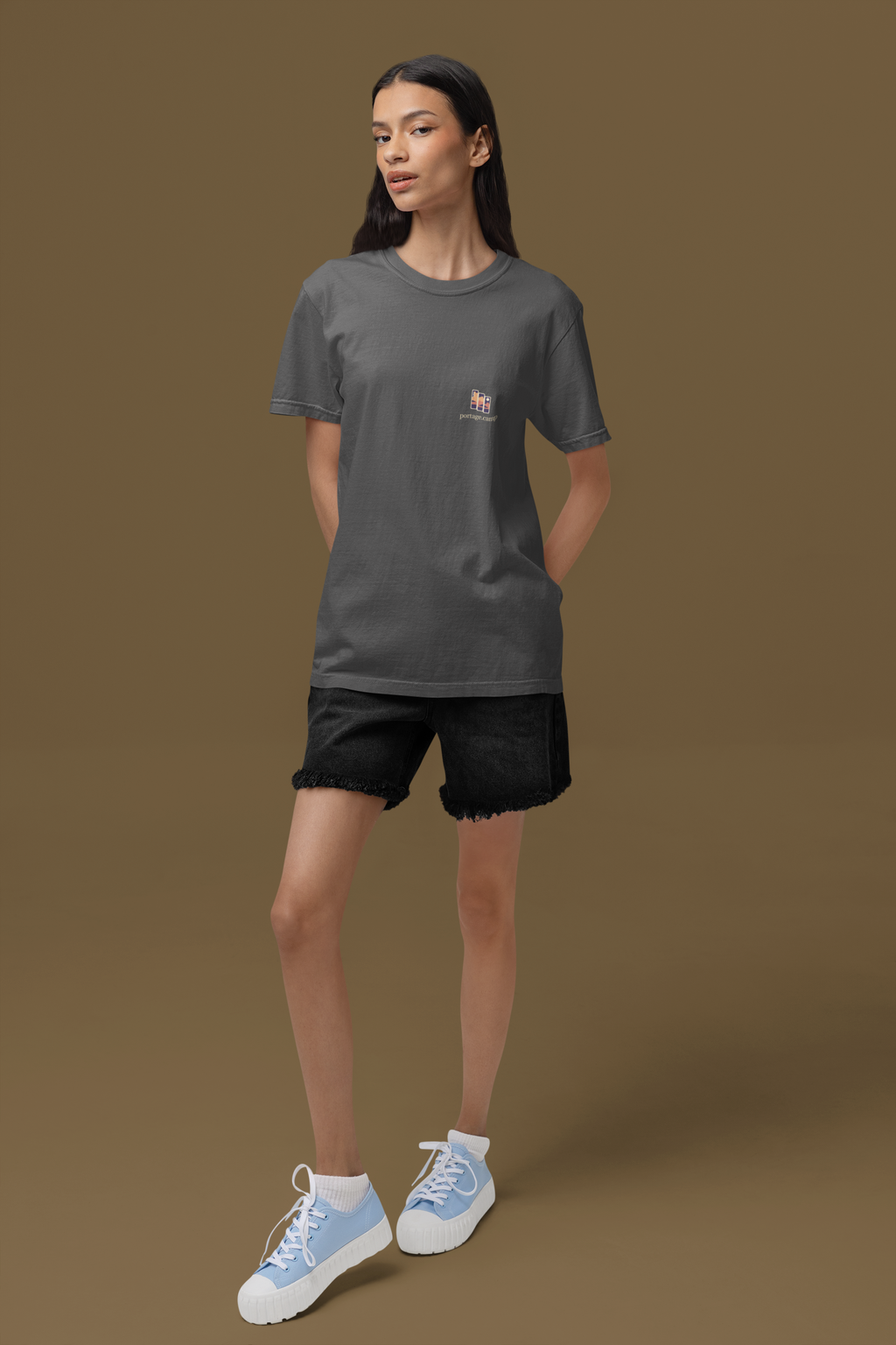 Stay for the Sky Garment-Dyed Tee in Graphite, worn by a woman standing in a studio, with the Stay for the Sky logo and portage.camp on the chest. Digital product mockup.