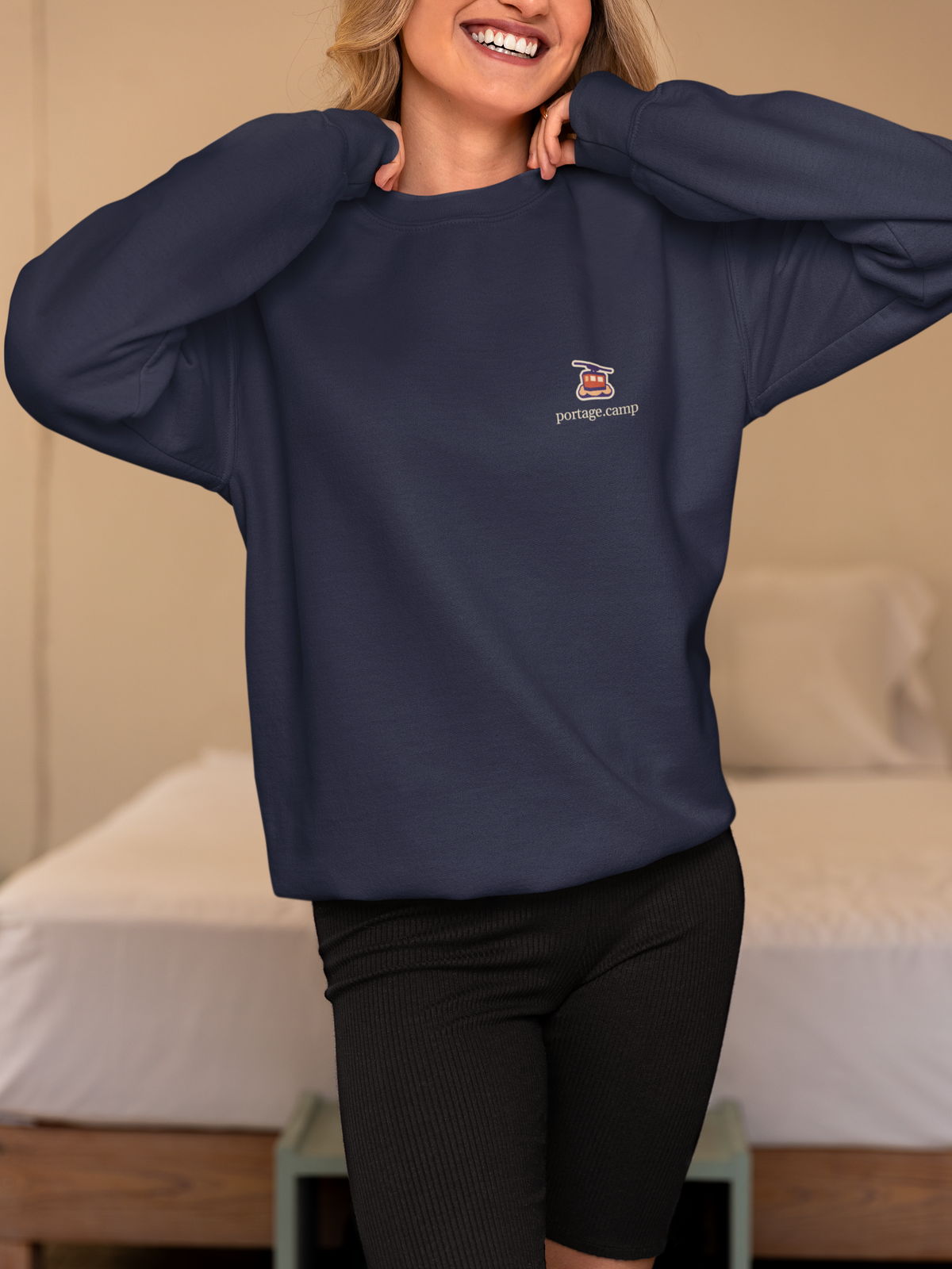 Cloud Ferry Garment-Dyed Crewneck in True Navy, worn by a woman in a bedroom, with the Cloud Ferry logo and portage.camp on the chest. Digital product mockup.