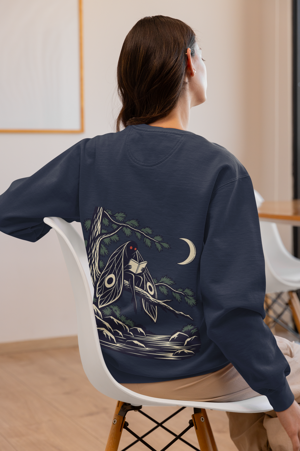 Night Library Garment-Dyed Crewneck in True Navy, worn by a woman seen from behind at home, showing the large print on the back. Digital product mockup.