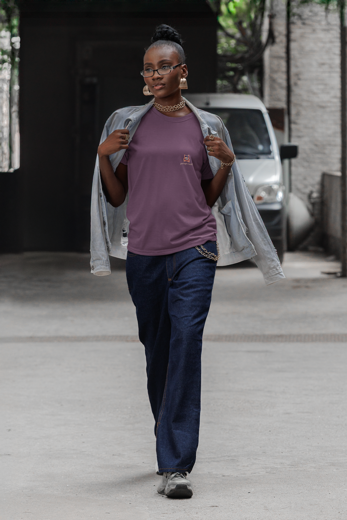 Edge of Evening Garment-Dyed Tee in Berry, worn by a woman walking down a city street, with the Edge of Evening logo and portage.camp on the chest. Digital product mockup.