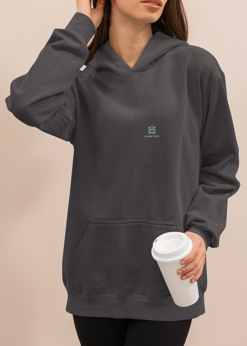 Night Library Midweight Hoodie in Black, worn by a woman at home with a coffee cup, with the Night Library logo and portage.camp on the chest. Digital product mockup.