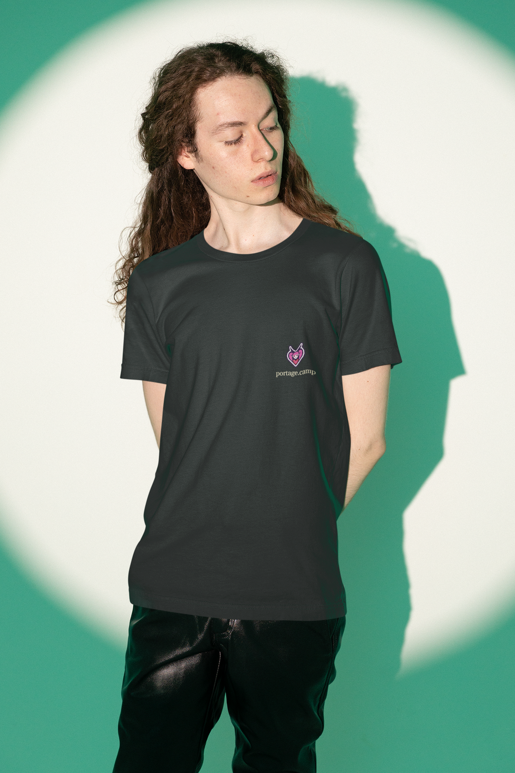 Heart Thief Garment-Dyed Tee in Black, worn by a man against green studio light, with the Heart Thief logo and portage.camp on the chest. Digital product mockup.