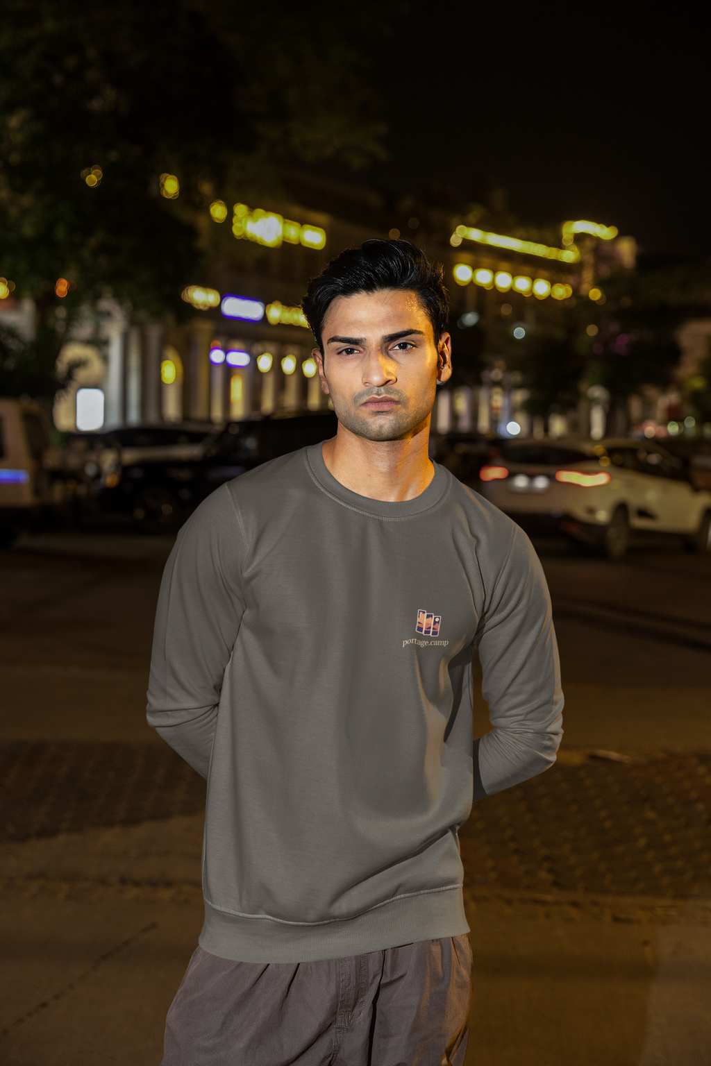 Stay for the Sky Garment-Dyed Crewneck in Pepper, worn by a man on a city street at night, with the Stay for the Sky logo and portage.camp on the chest. Digital product mockup.
