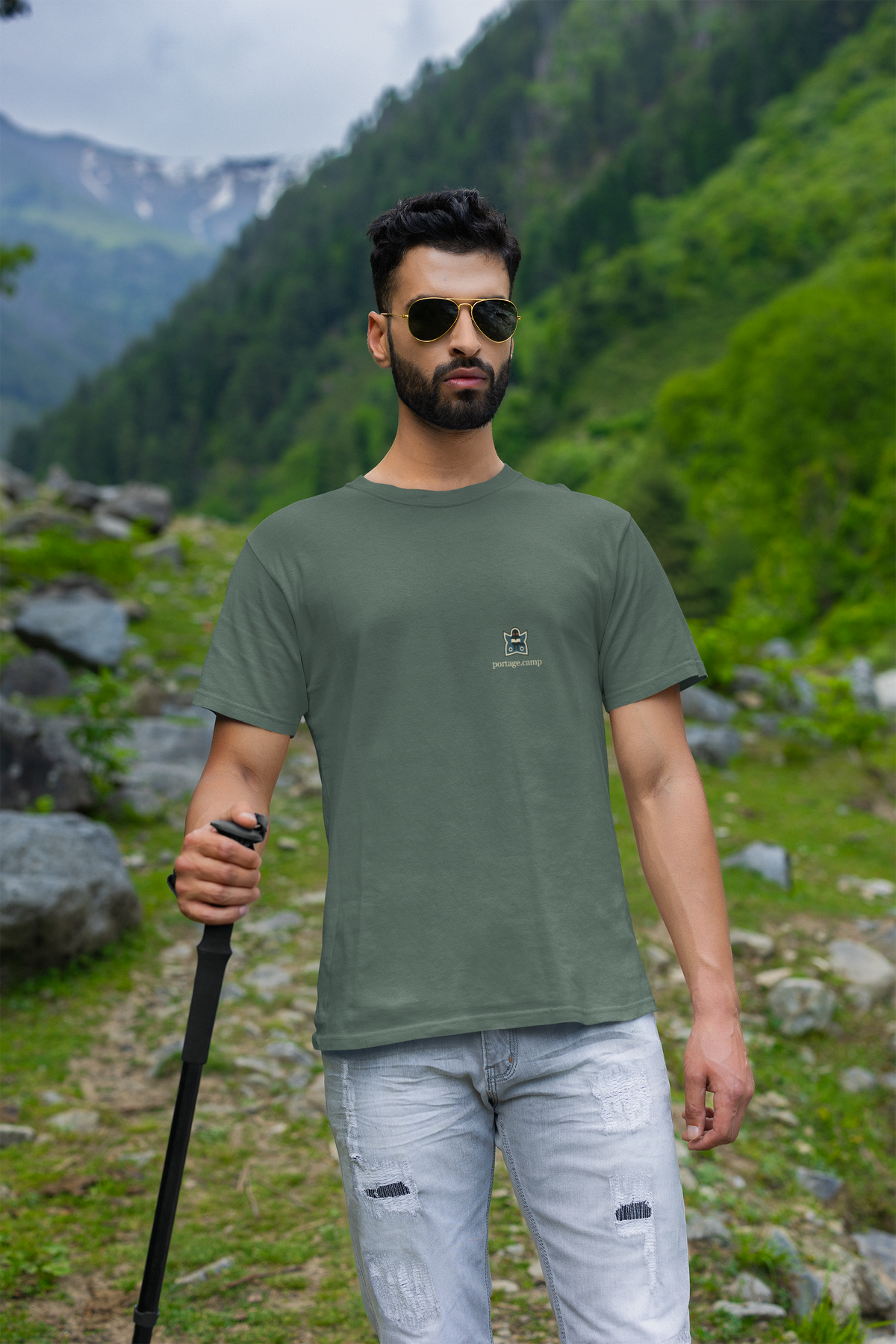 Night Library Garment-Dyed Tee in Blue Spruce, worn by a man on a mountain trail, with the Night Library logo and portage.camp on the chest. Digital product mockup.