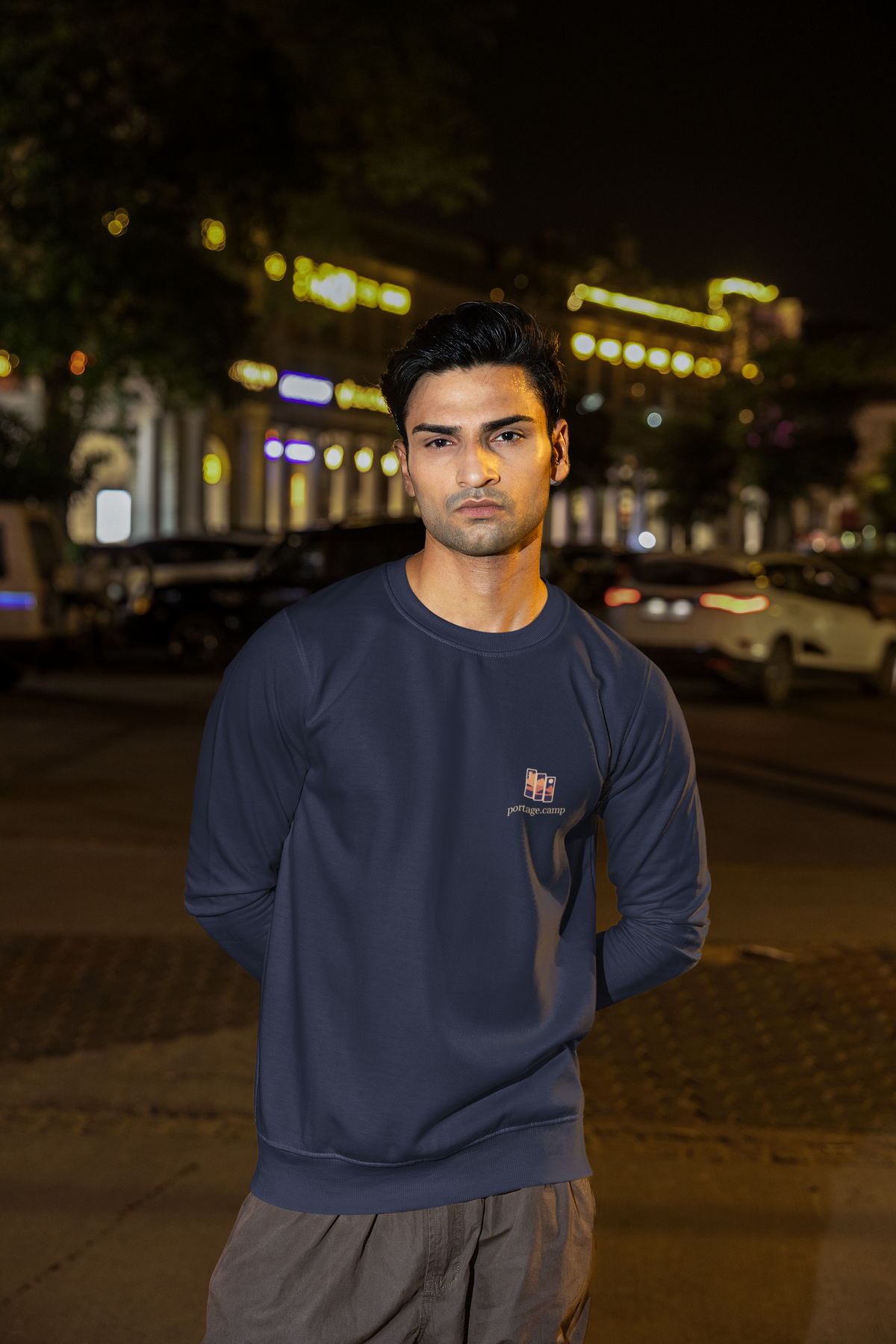 Stay for the Sky Garment-Dyed Crewneck in True Navy, worn by a man on a city street at night, with the Stay for the Sky logo and portage.camp on the chest. Digital product mockup.