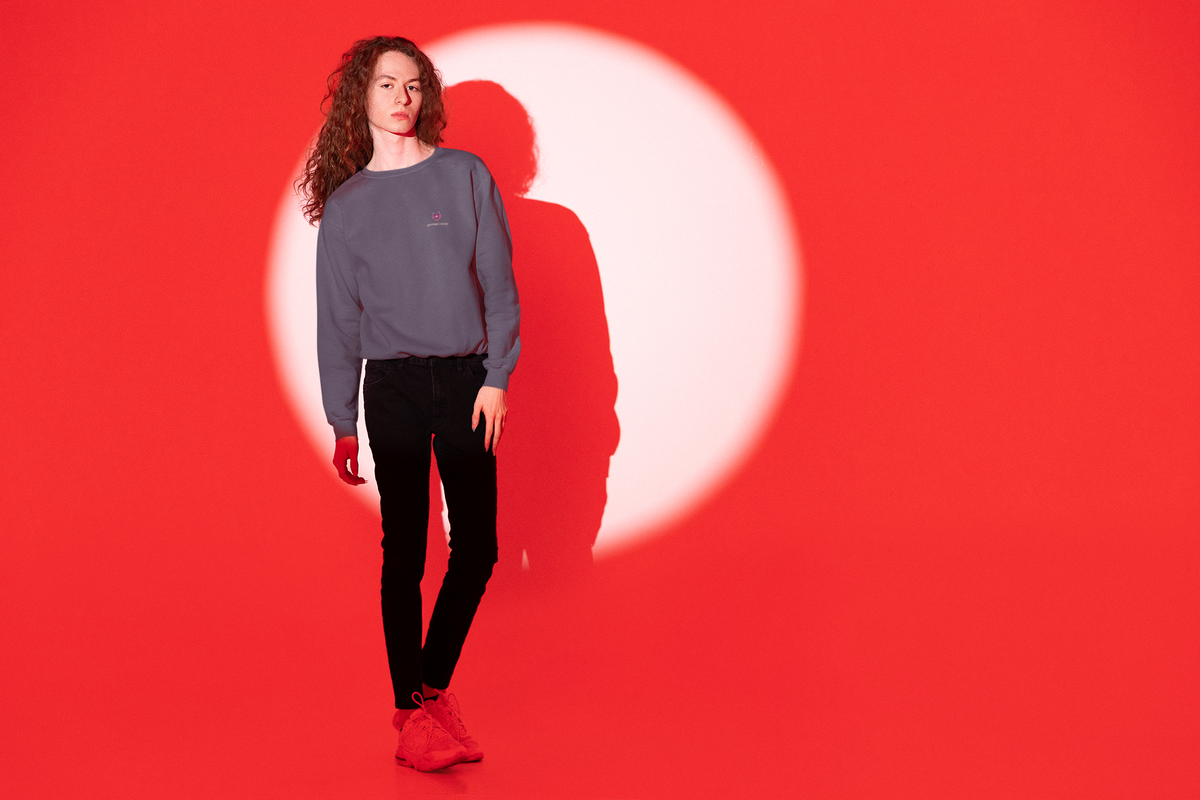 Heart Thief Garment-Dyed Crewneck in Denim, worn by a man against a red light, with the Heart Thief logo and portage.camp on the chest. Digital product mockup.