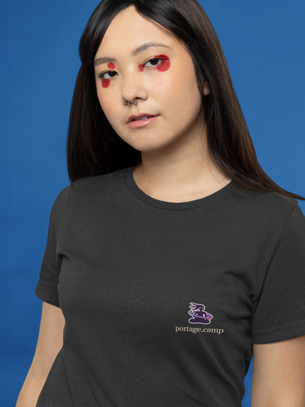 Orbit Keeper Garment-Dyed Tee in Black, worn by a woman with graphic eyeliner, close up, with the Orbit Keeper logo and portage.camp on the chest. Digital product mockup.