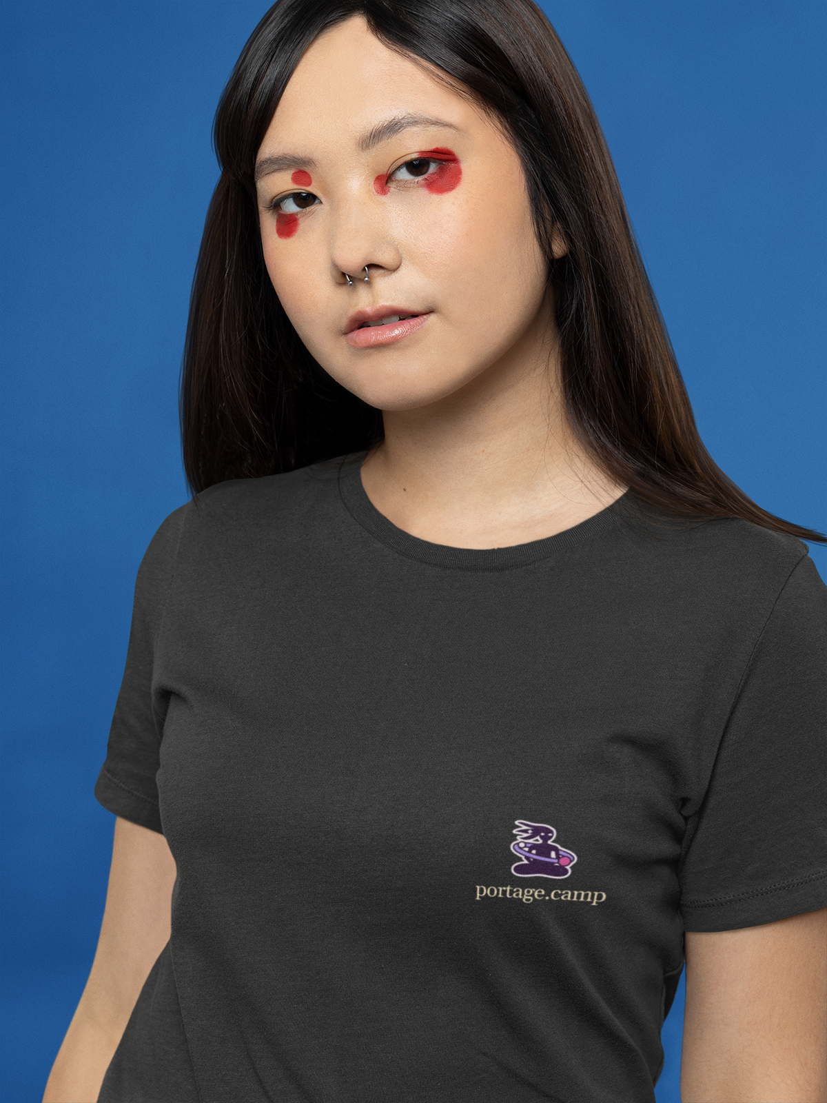 Orbit Keeper Garment-Dyed Tee in Black, worn by a woman with graphic eyeliner, close up, with the Orbit Keeper logo and portage.camp on the chest. Digital product mockup.