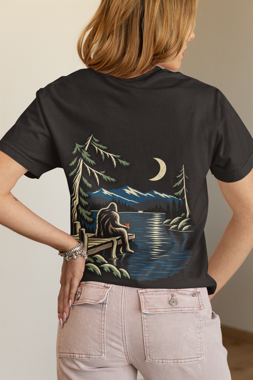 Quiet Hours Garment-Dyed Tee in Black, worn by a woman seen from behind in a bedroom at home, showing the large print on the back. Digital product mockup.