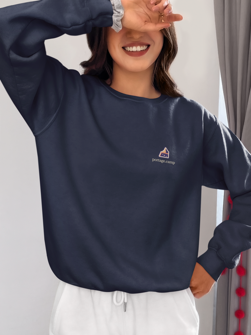 A Different Sky Garment-Dyed Crewneck in True Navy, worn by a woman at home, with the A Different Sky logo and portage.camp on the chest. Digital product mockup.