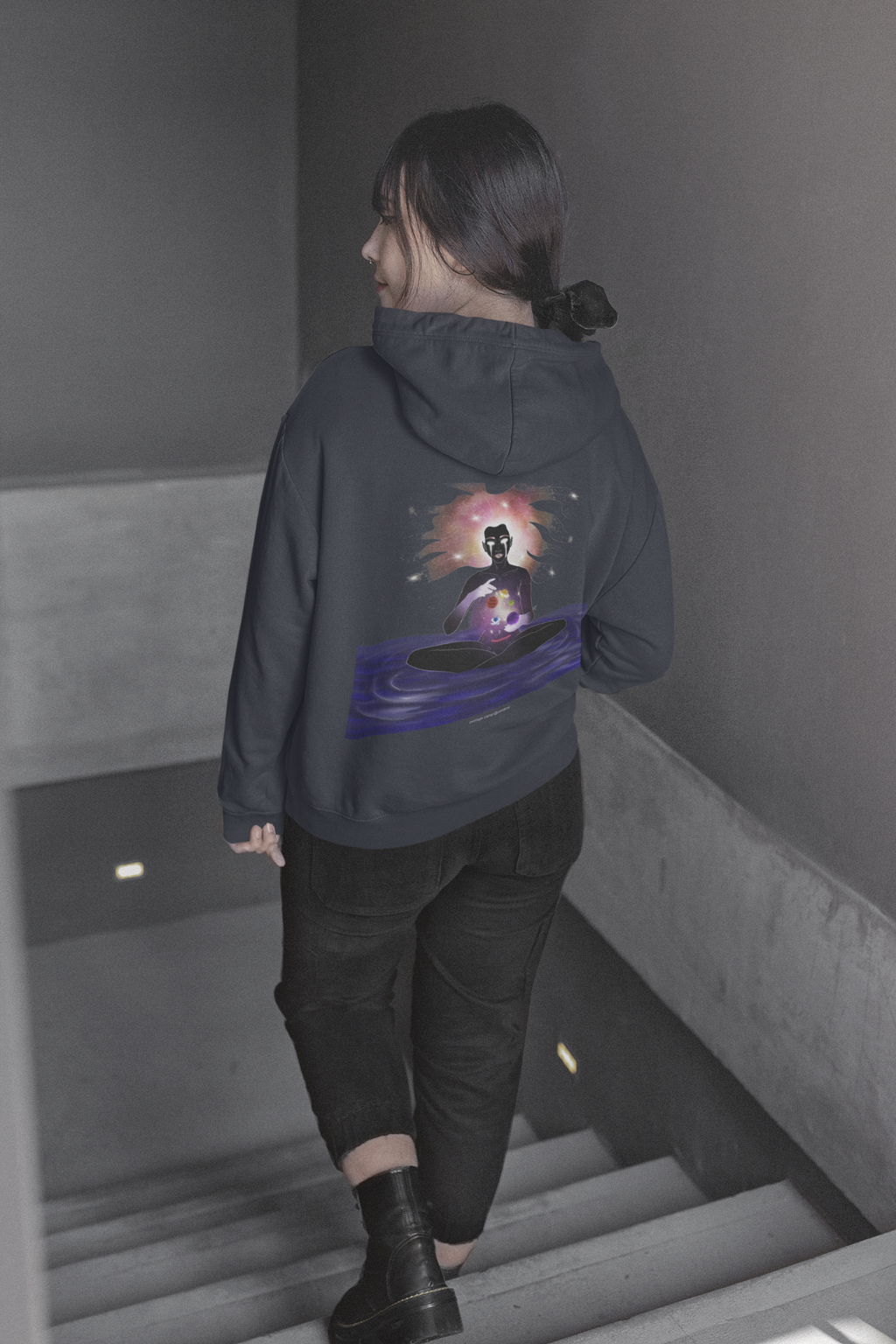 Orbit Keeper Midweight Hoodie in Classic Navy, worn by a woman seen from behind walking down a staircase, showing the large print on the back. Digital product mockup.