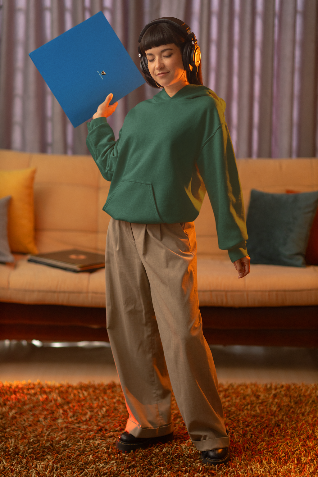 Seen Briefly Midweight Hoodie in Alpine Green, worn by a woman in headphones, holding a record sleeve, with the Seen Briefly logo and portage.camp on the chest. Digital product mockup.
