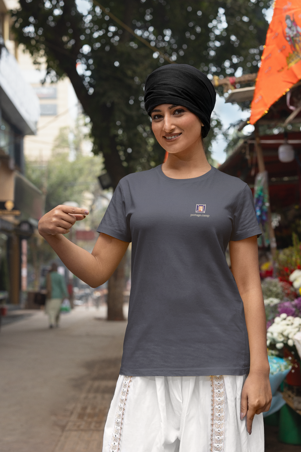 Open Late Garment-Dyed Tee in Navy, worn by a woman in a turban by a flower market, with the Open Late logo and portage.camp on the chest. Digital product mockup.