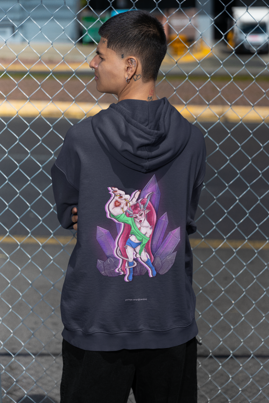 Amethyst After Hours Midweight Hoodie in Classic Navy, worn by a man seen from behind by a chain-link fence, showing the large print on the back. Digital product mockup.